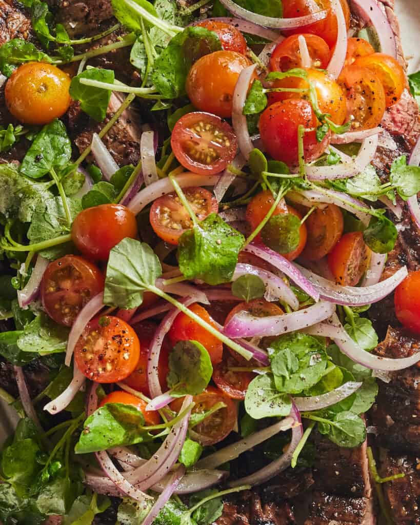 A close up shot of a grilled skirt steak topped with a cherry tomato salad.