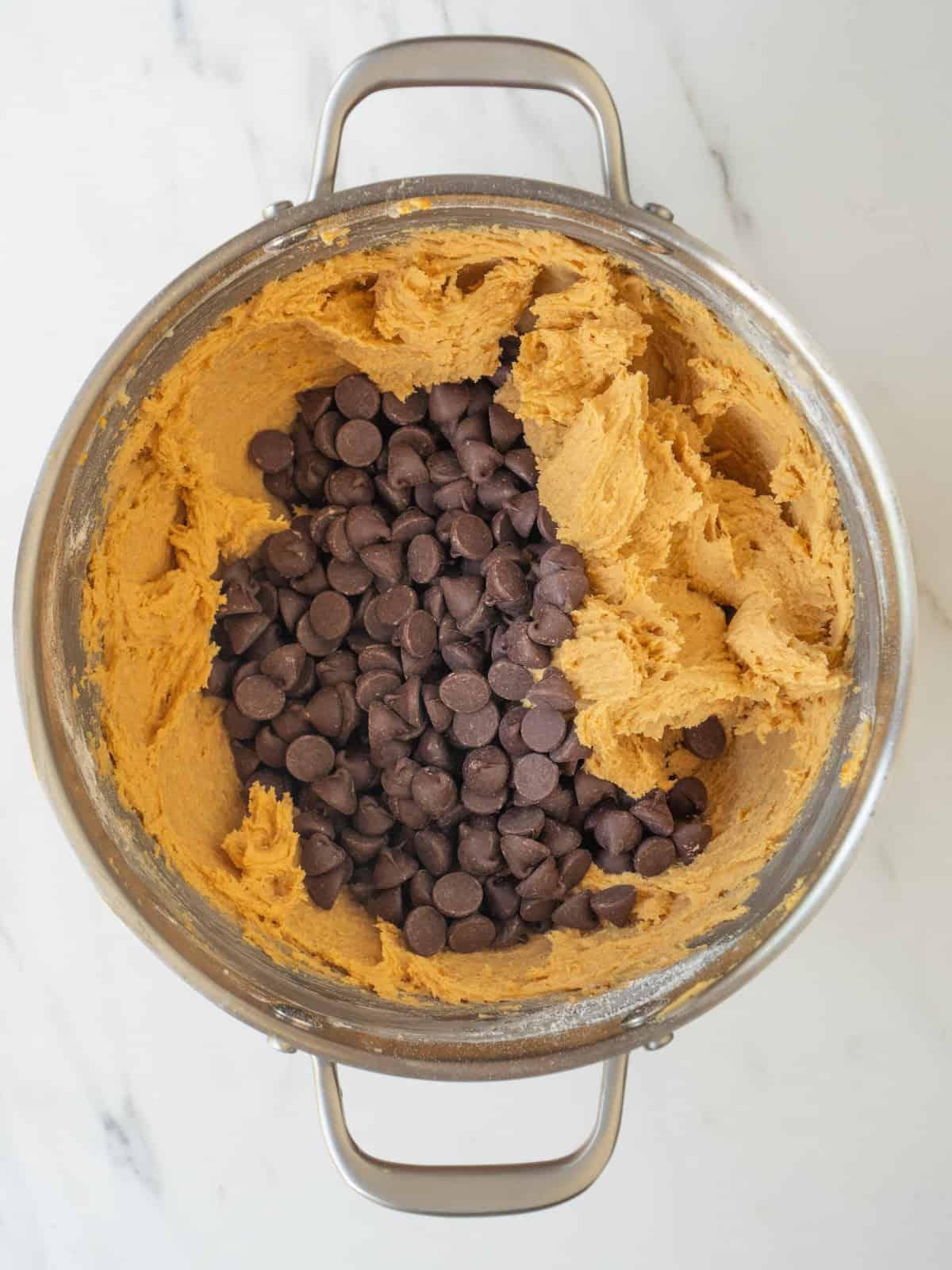 A stand mixer bowl with cookie dough and chocolate chips added to it.