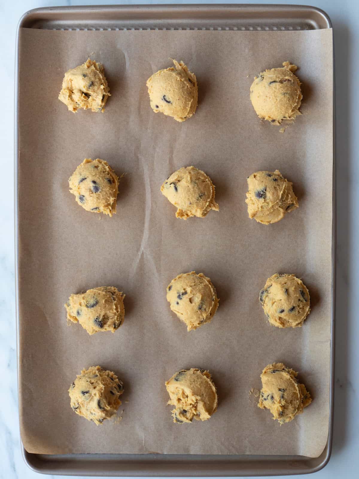 A baking sheet lined with parchment paper with twelve cookie dough balls scooped onto it ready to be baked.