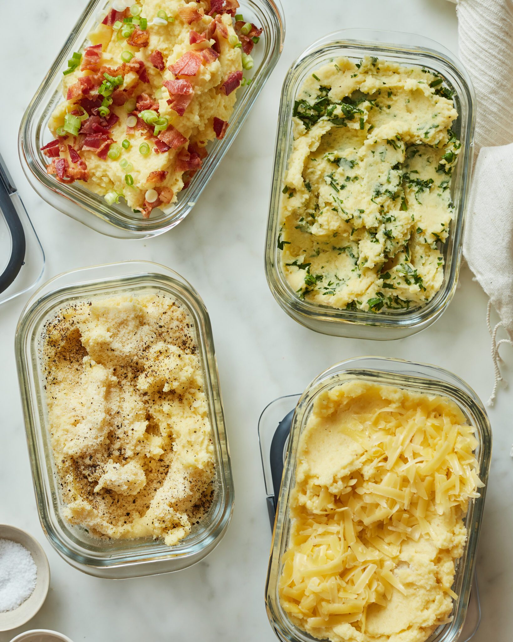 4 different dishes of mashed potatoes.  One dish is bacon and scallion mashed potatoes, one dish is herby olive oil mashed potatoes, one dish is cacio e pepe mashed potatoes, and one dish is white cheddar mashed potatoes.  