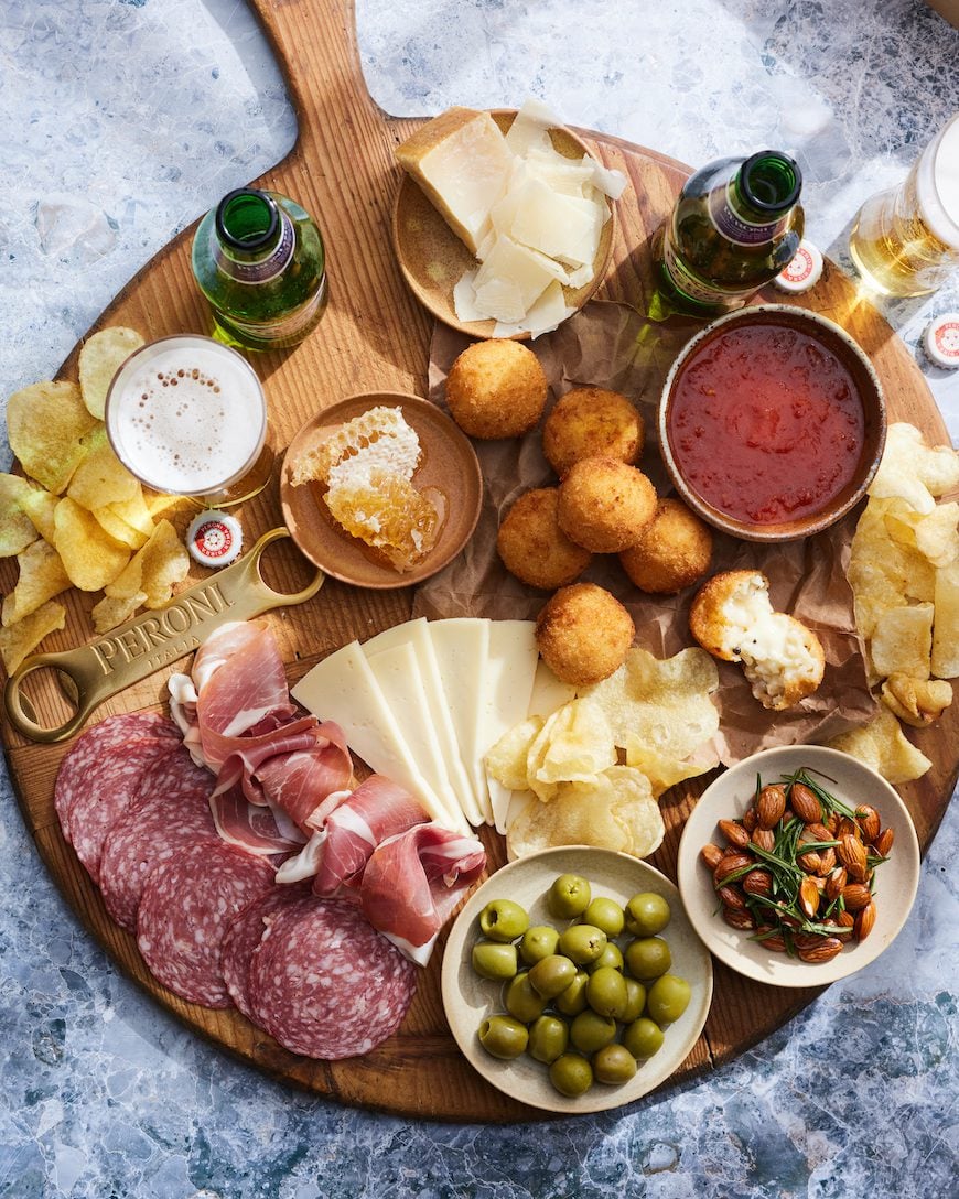 New Year's Eve Food Parmesan Arancini Board with chips, salami, prosciutto, olives, almonds, marinara sauce, and bottles of beer