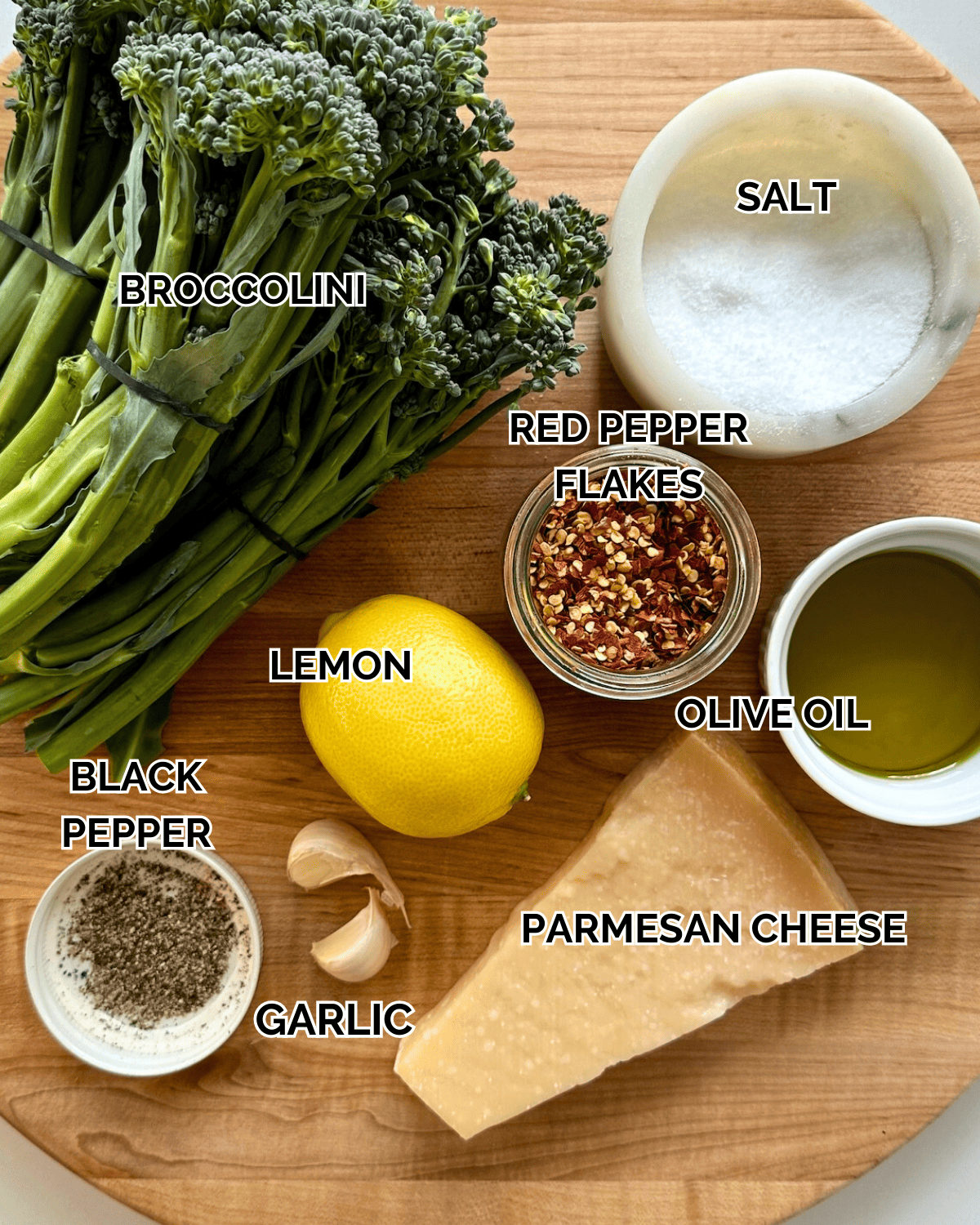 Roasted Broccolini Ingredients: Broccolini, olive oil. salt, pepper, parmesan cheese, garlic cloves, lemon, red pepper flakes all prepped out on a wooden cutting board
