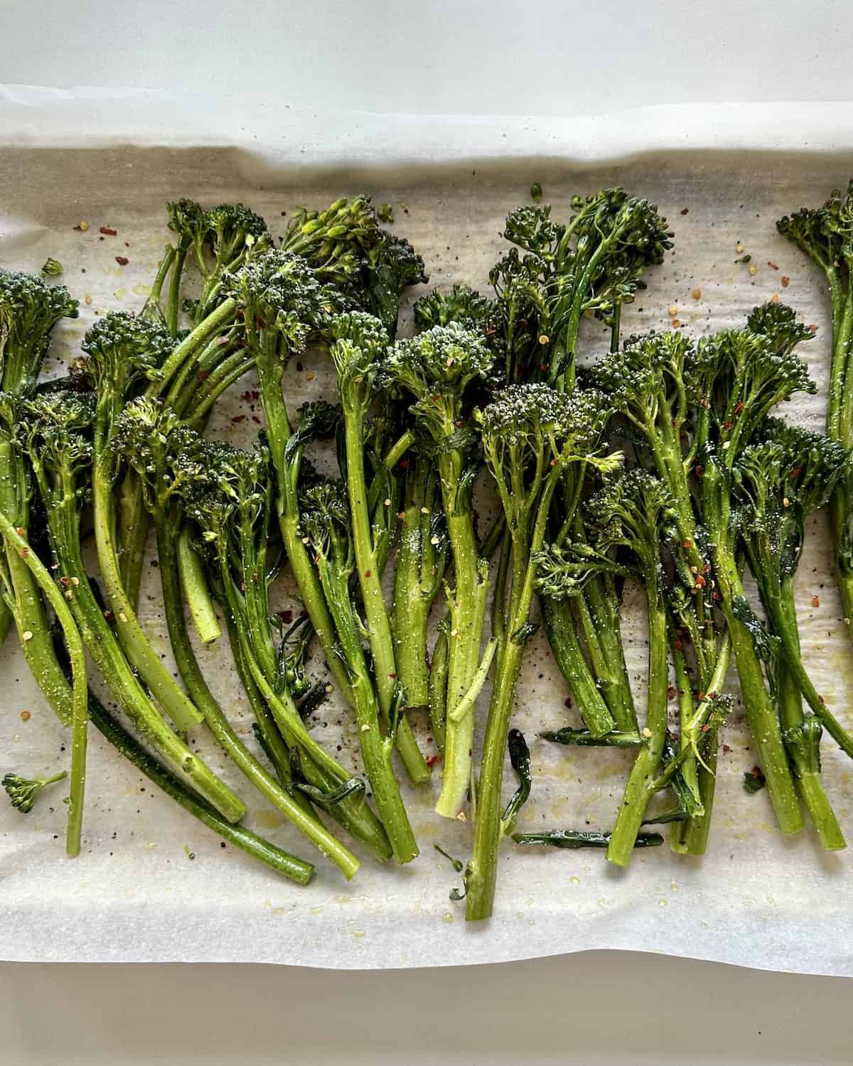a  baking sheet lined with parchment paper with broccolini spread evenly on the baking sheet and tossed with olive oil salt pepper and red pepper flakes.