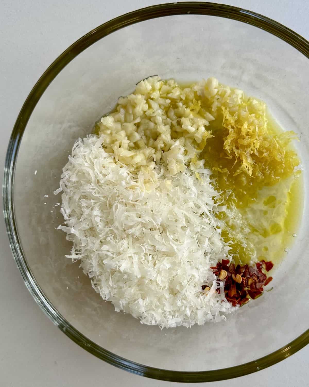 live oil, minced garlic, red pepper flakes, lemon zest and juice and grated parmesan in a clear bowl.
