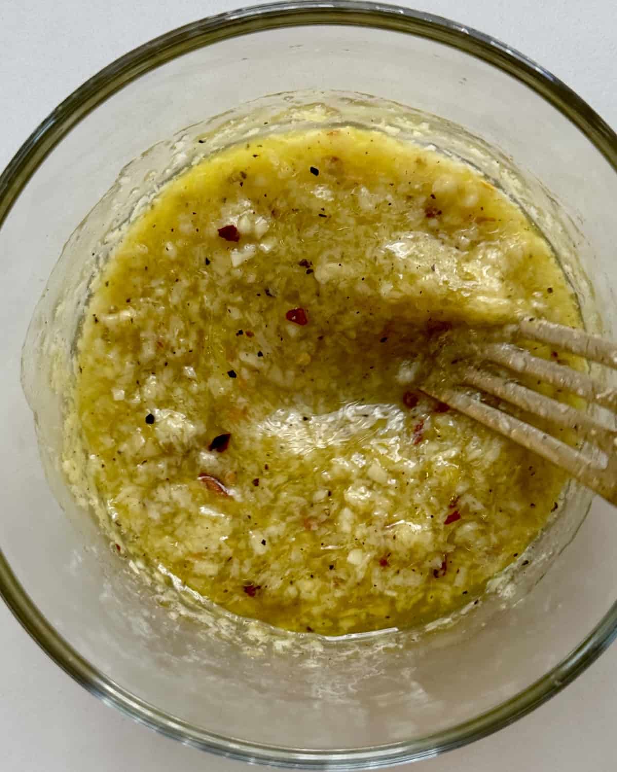 Olive oil, minced garlic, red pepper flakes, lemon zest and juice and grated parmesan mixed together in a clear bowl.