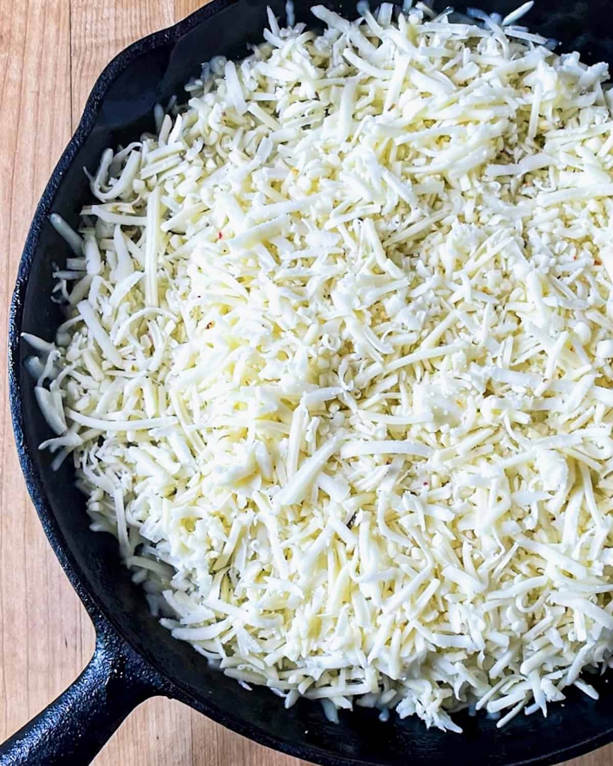 A skillet with a layer of shredded cheese covering sautéed onions and peppers underneath. 