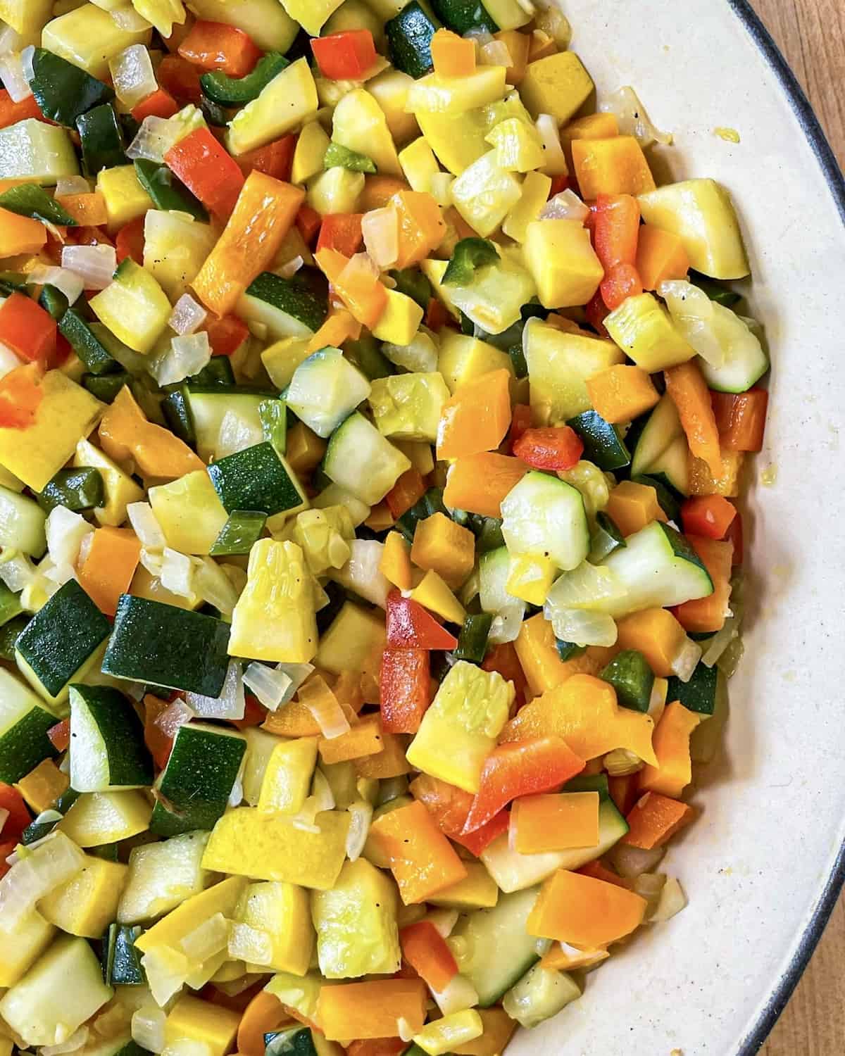 A mixture of diced onions, poblano peppers, bell peppers, zucchini, and yellow squash that have been cooked until soft in a skillet.