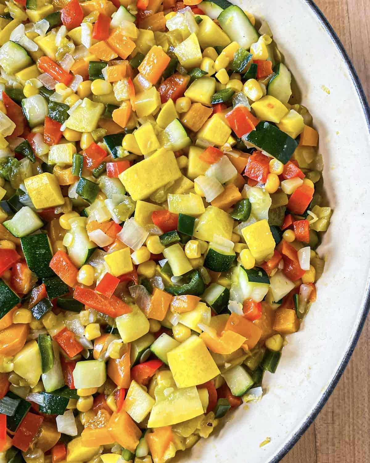 A mixture of diced onions, poblano peppers, bell peppers, zucchini, yellow squash, corn, and green chiles that have been cooked until soft in a skillet.