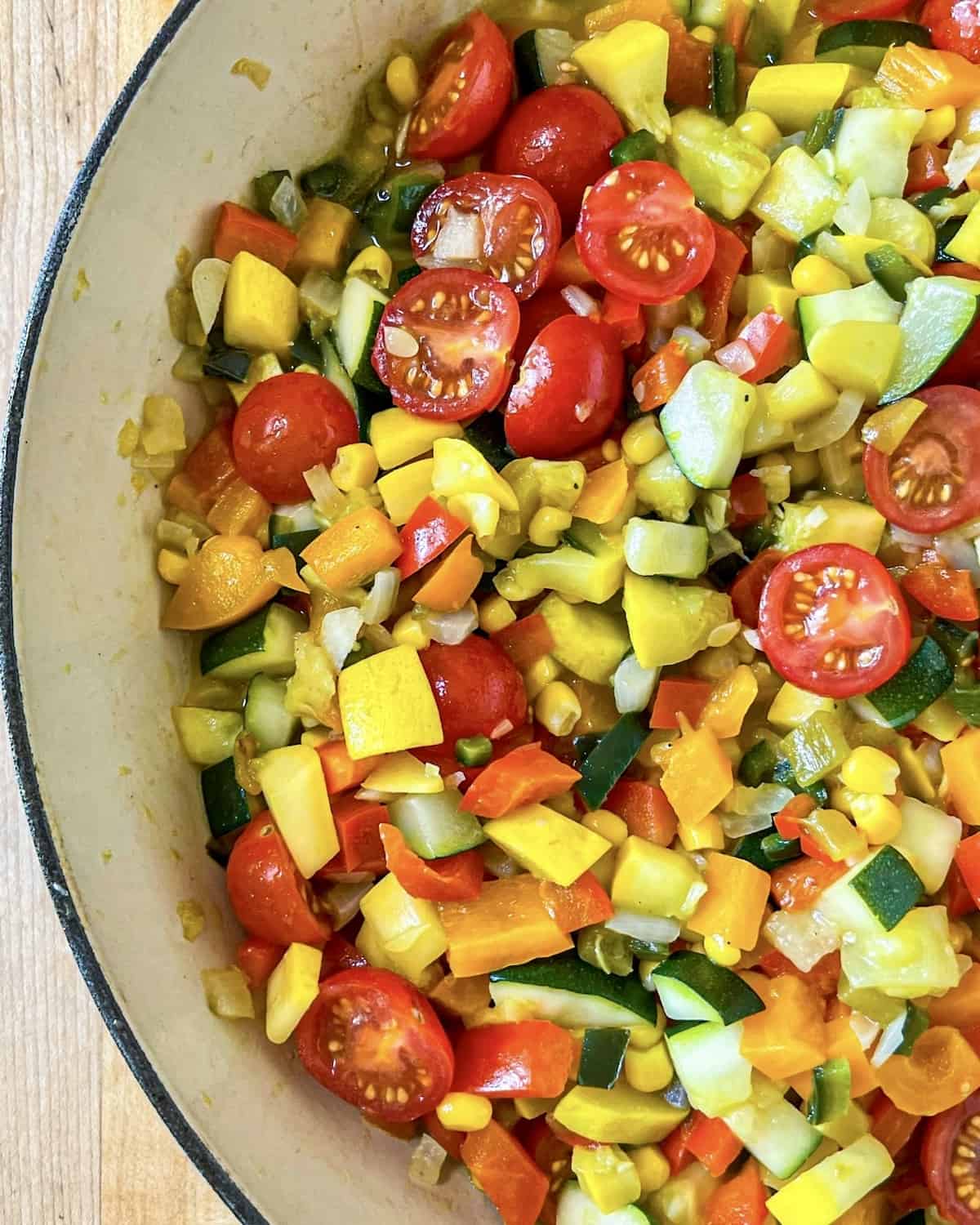 A mixture of diced onions, poblano peppers, bell peppers, zucchini, yellow squash, corn, green chiles, and cherry tomatoes that have been cooked until soft in a skillet.