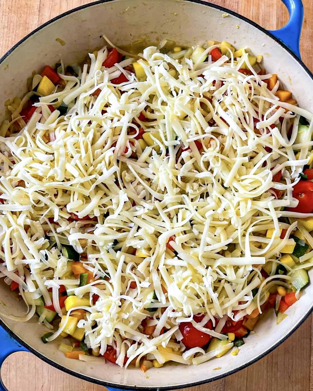 A mixture of diced onions, poblano peppers, bell peppers, zucchini, yellow squash, corn, green chiles, and cherry tomatoes that have been cooked until soft in a skillet and topped with shredded cheddar cheese/