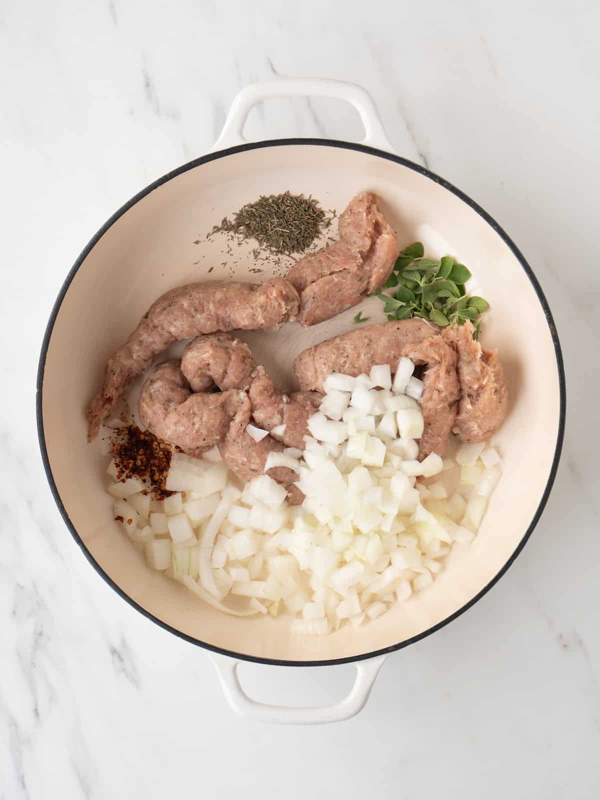 A dutch oven with chopped onions, chicken sausage and herbs being sautéed.