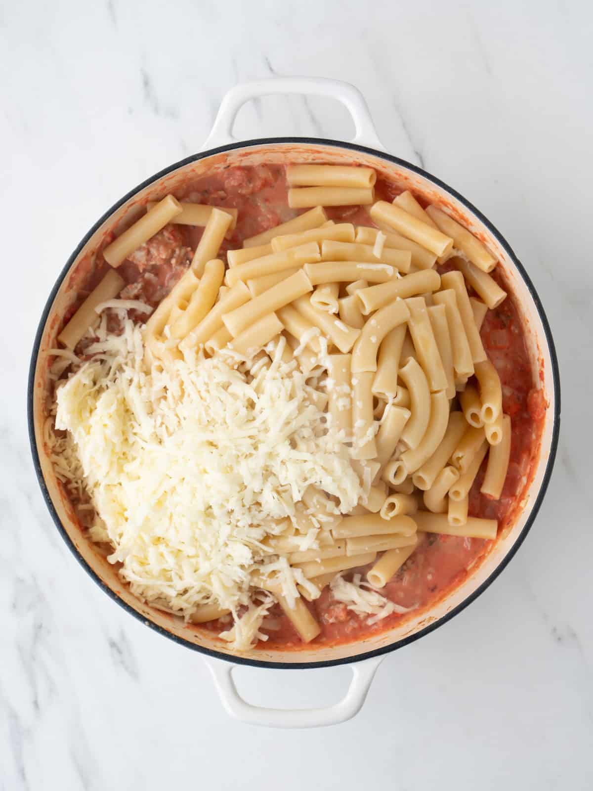 A dutch oven with a tomato sauce with chicken sausage, and boiled pasta and shredded mozzarella added to it.