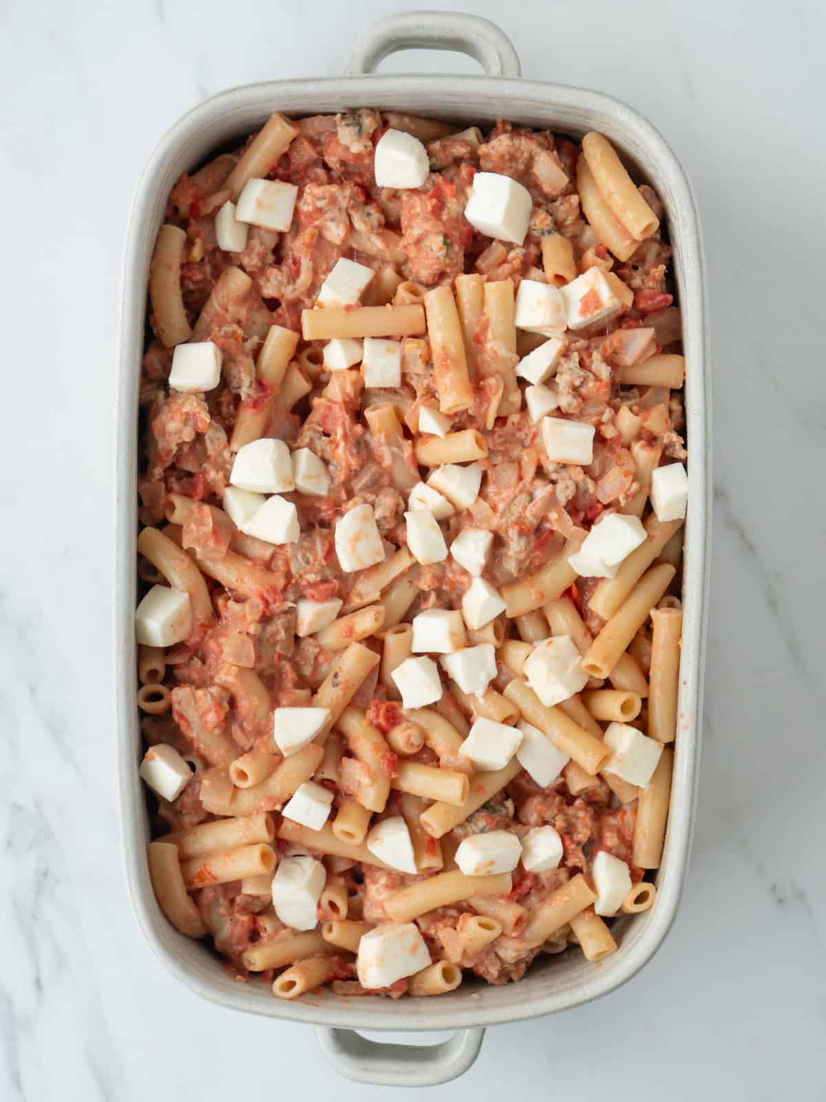 A casserole dish with the chicken sausage pasta added to it, and topped with pieces of mozzarella cheese, ready to be baked.