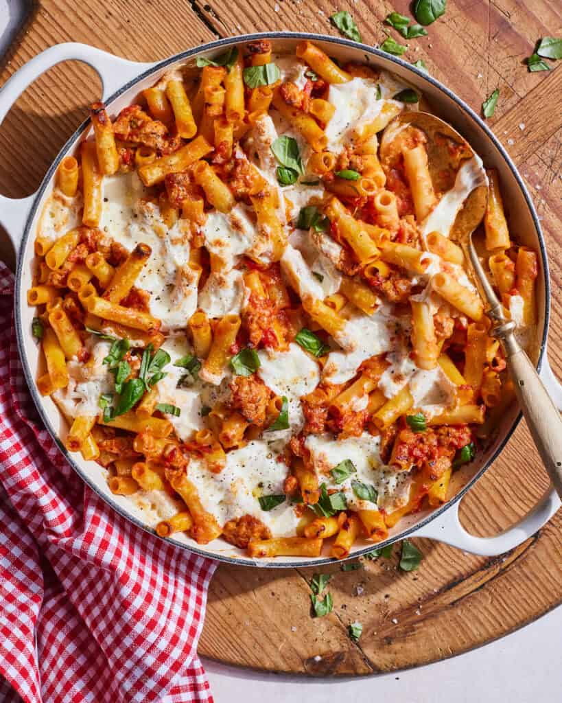 A skillet with cheesy chicken sausage pasta bake on a wooden platter.