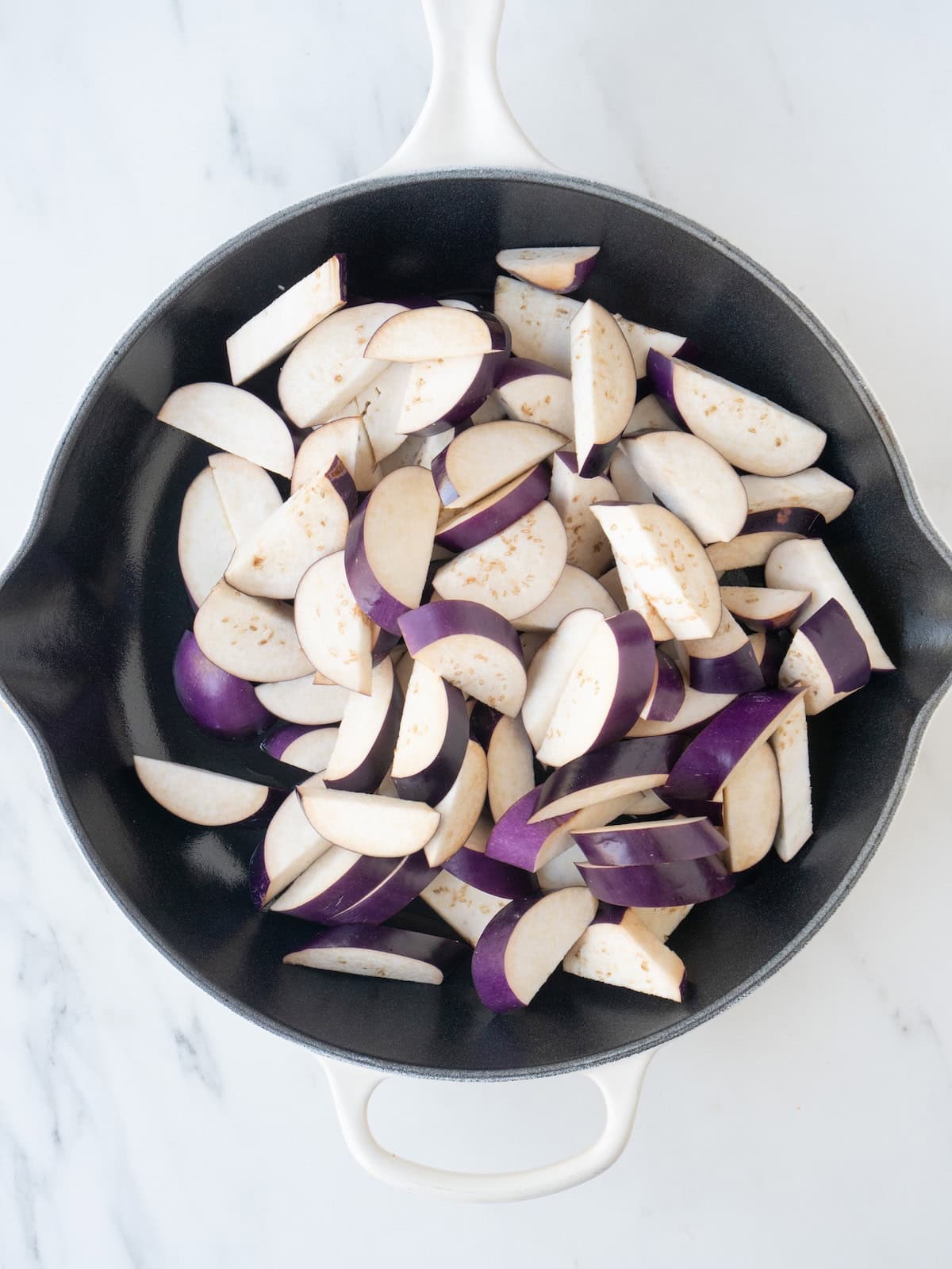 A skillet with chopped eggplant being sautéed in some oil.