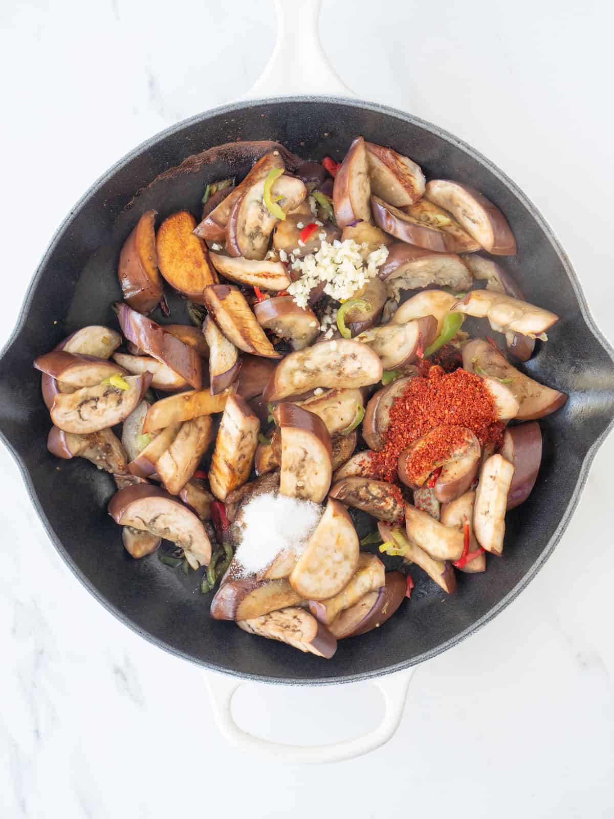 A skillet with stir fried eggplant being cooked, with korean red chili flakes, sugar, garlic and soy sauce added.