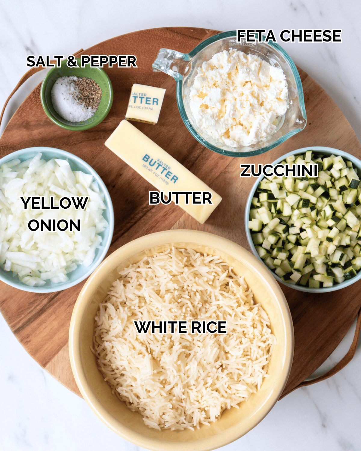 Crispy Rice Ingredients: Feta cheese, yellow onion, white rice, zucchini, butter, salt and pepper measured out and prepped on a wooden cutting board