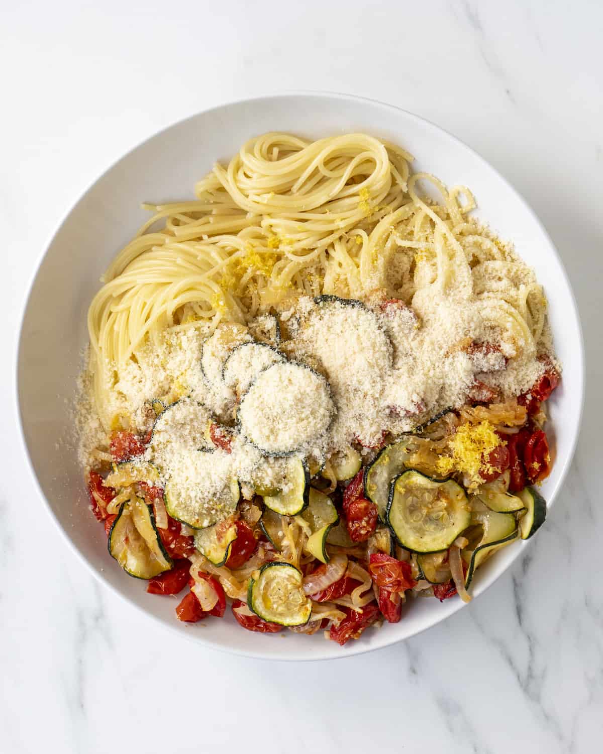 A bowl of cooked spaghetti, parmesan cheese, and roasted vegetables. 
