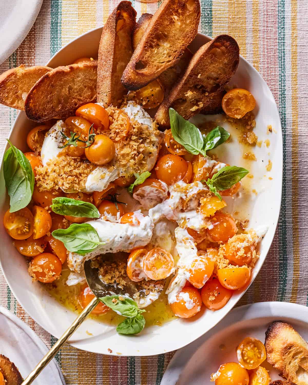A plate with halved cherry tomatoes, balls of burrata, slices of toasted bred, and leaves of basil.  