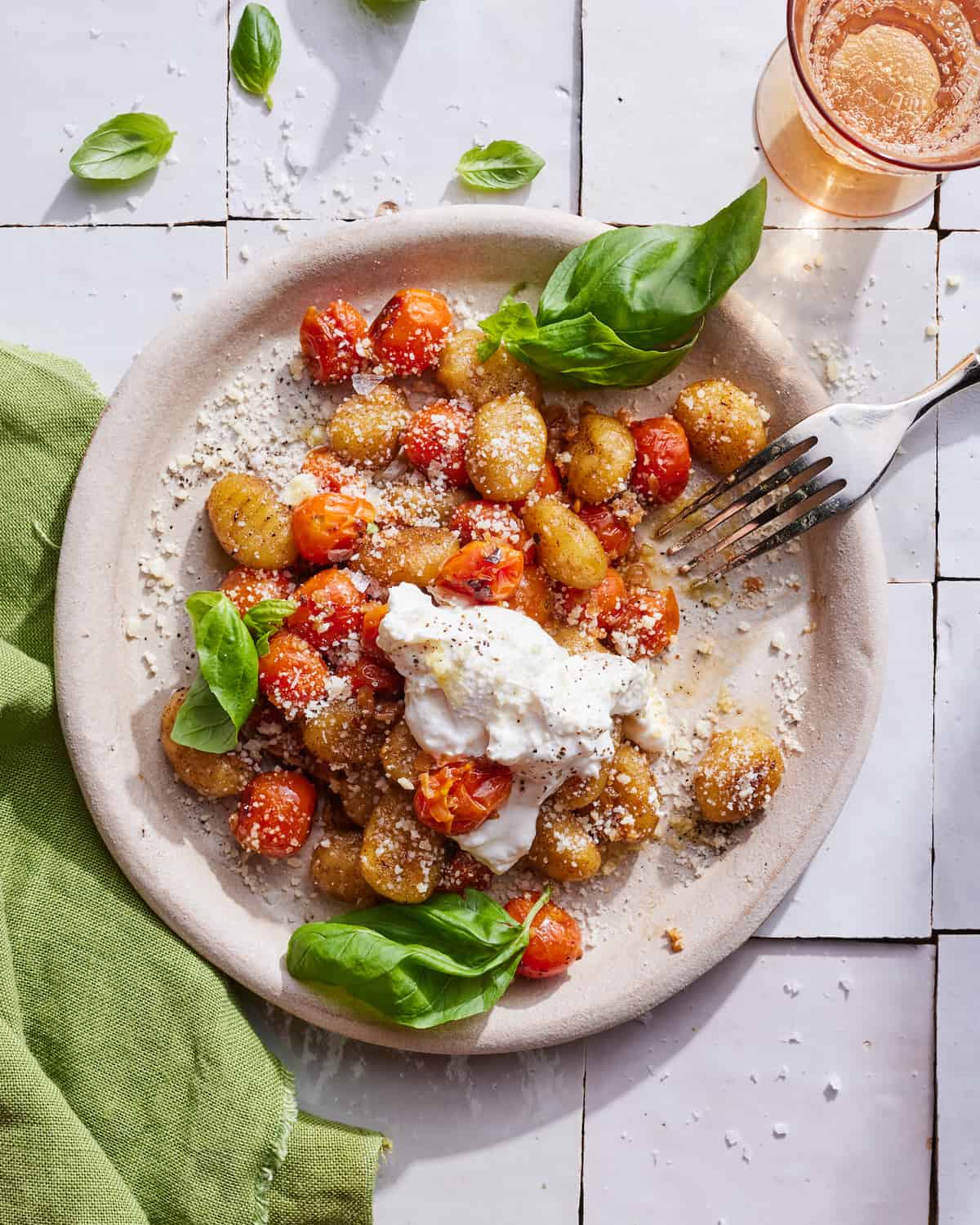 A round plate of crispy tomato basil gnocchi with a big chunk of burrata on a white tile table