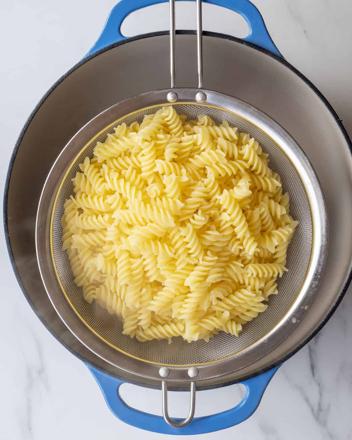 Pasta, sitting in a strainer sitting over a dutch oven.  
