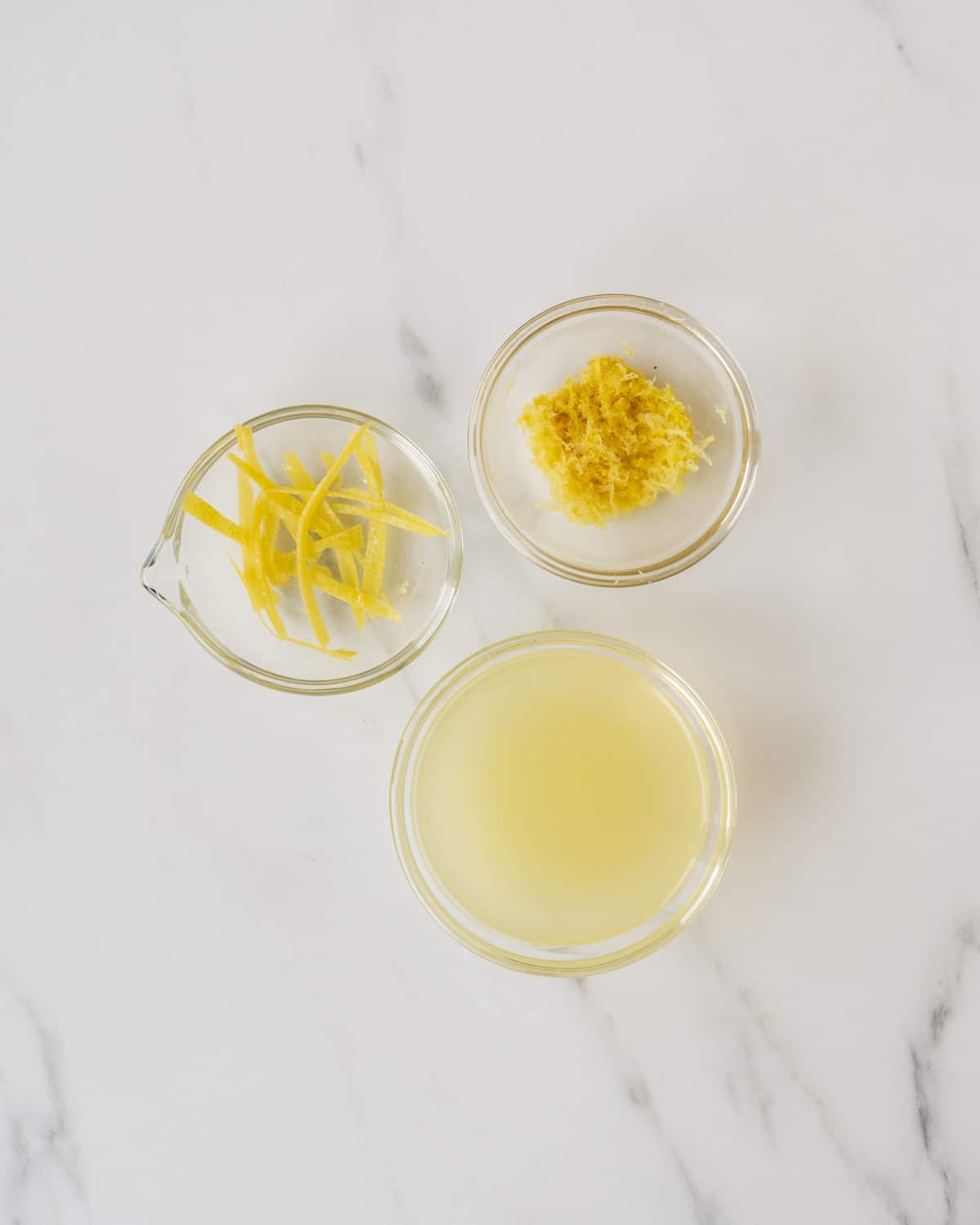 A bowl of lemon zest, a bowl of lemon peel strands, and a bowl of lemon juice.  