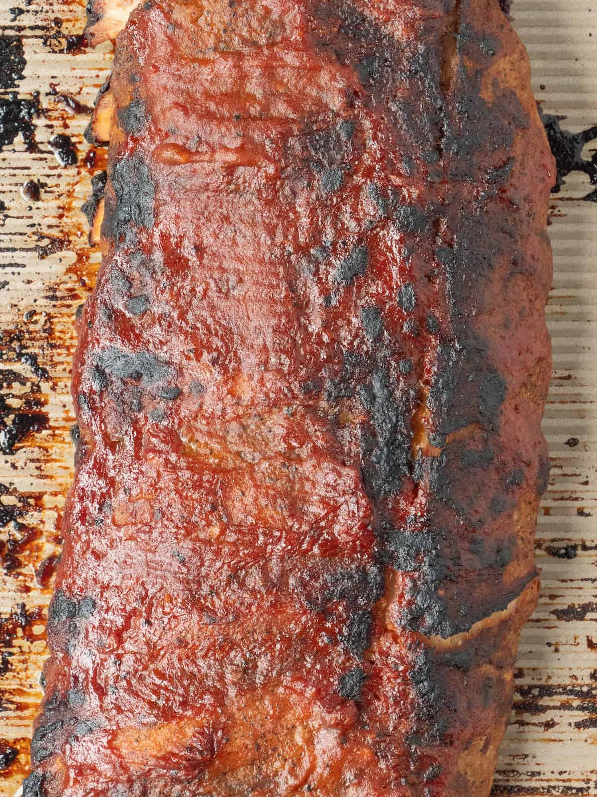 A close up of a baking sheet with a broiled spiced bbq baby back rack of ribs, broiled or grilled with browned crispy spots.