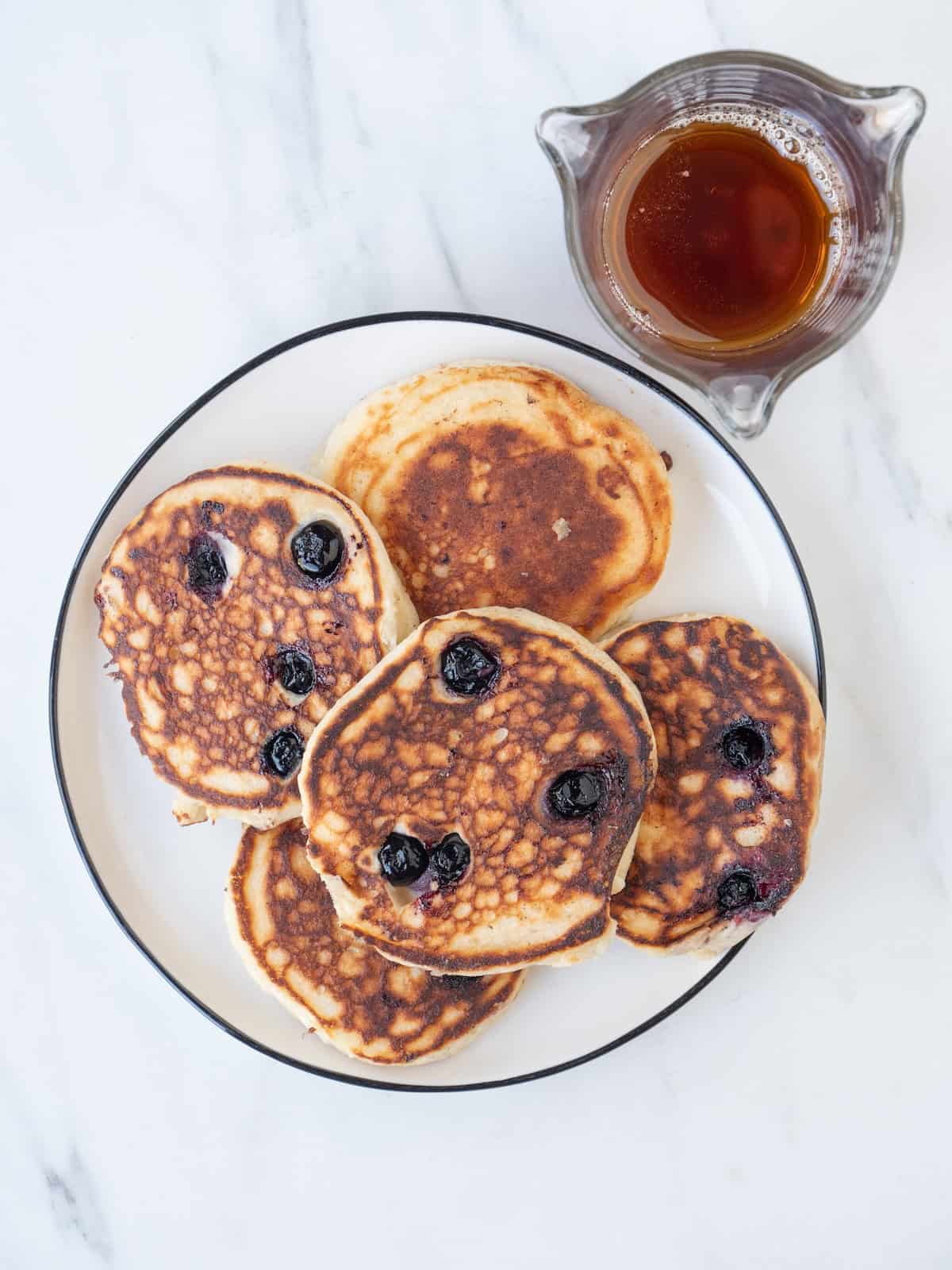 A plate with five blueberry buttermilk pancakes with a bowl of maple syrup on the side.