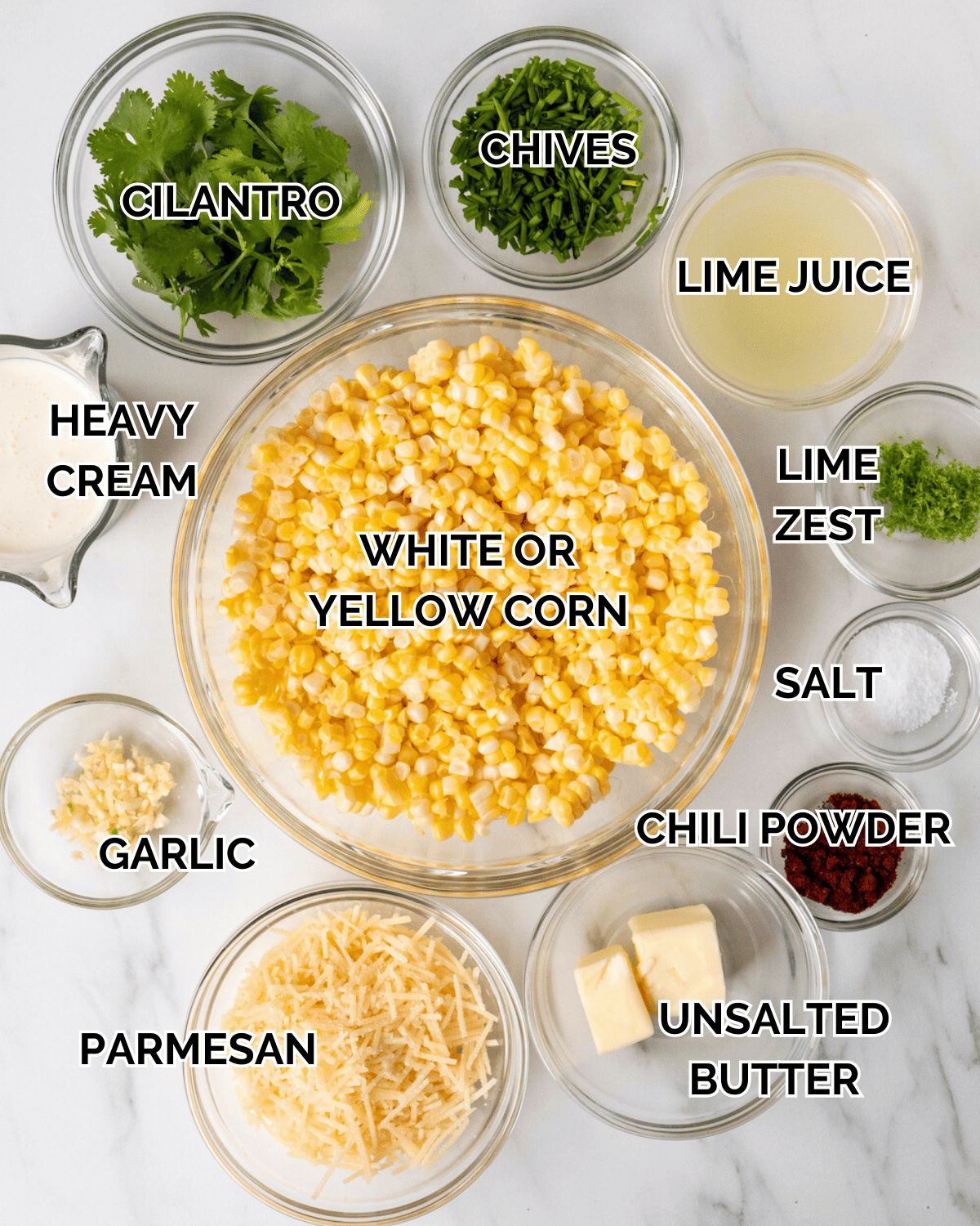 An overhead shot of all the ingredients in prep bowls. Ingredients consists of cilantro, chives, lime juice, heavy cream, white corn, lime zest, garlic, parmesan, unsalted butter, chili powder, and salt.  