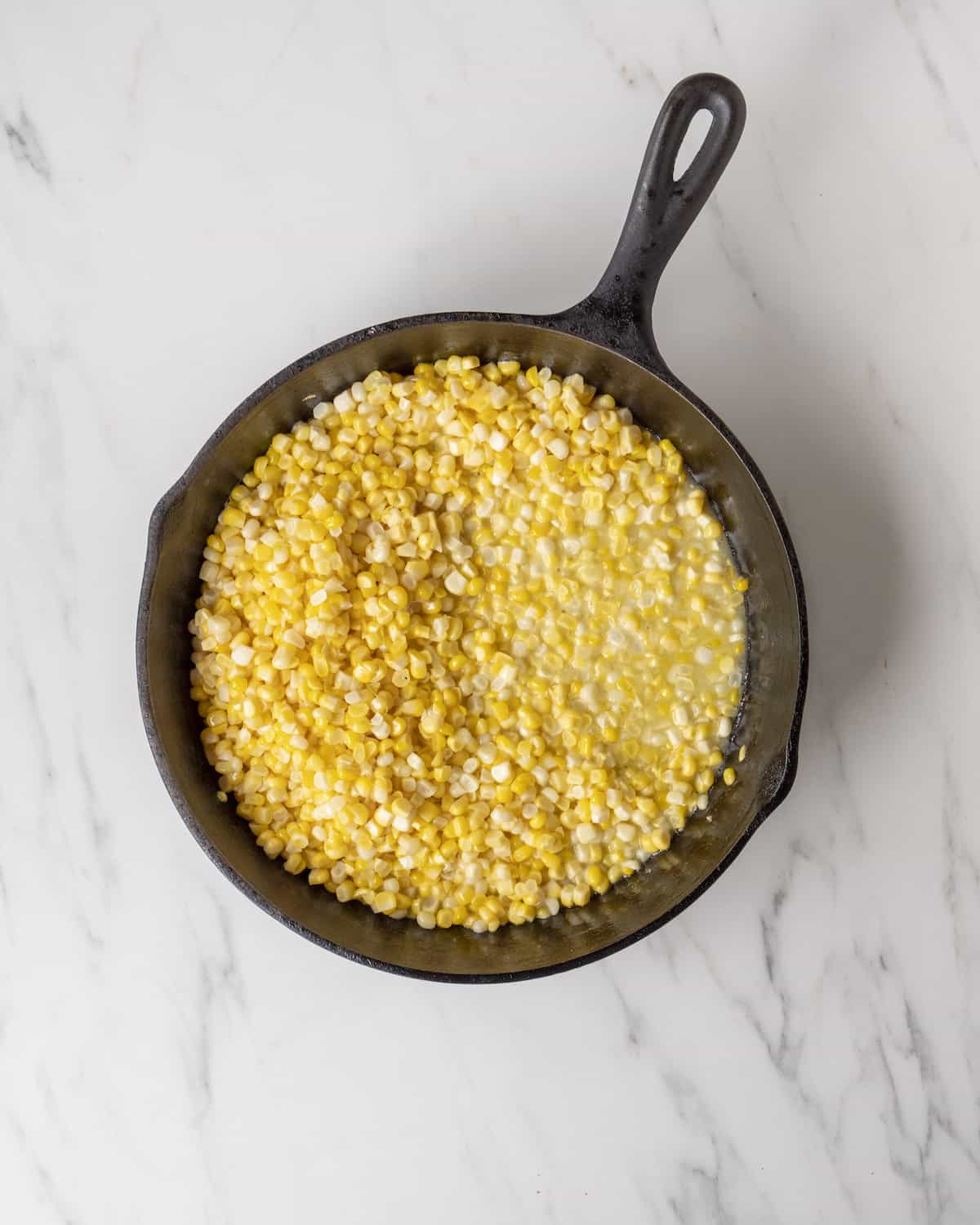 A skillet with melted butter and uncooked yellow corn.