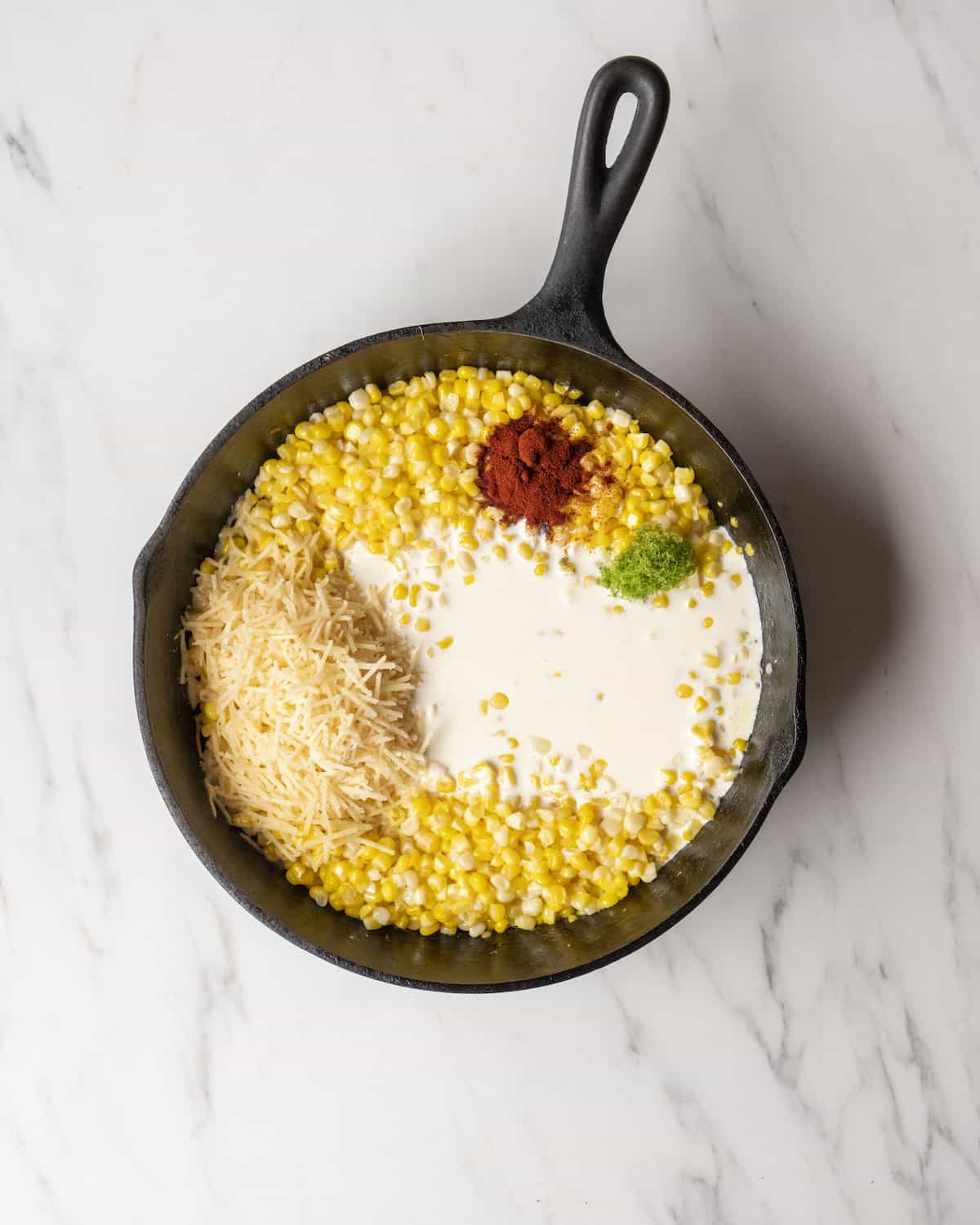 A skillet with cooked corn, heavy cream, chili powder, parmesan, and lime zest.  