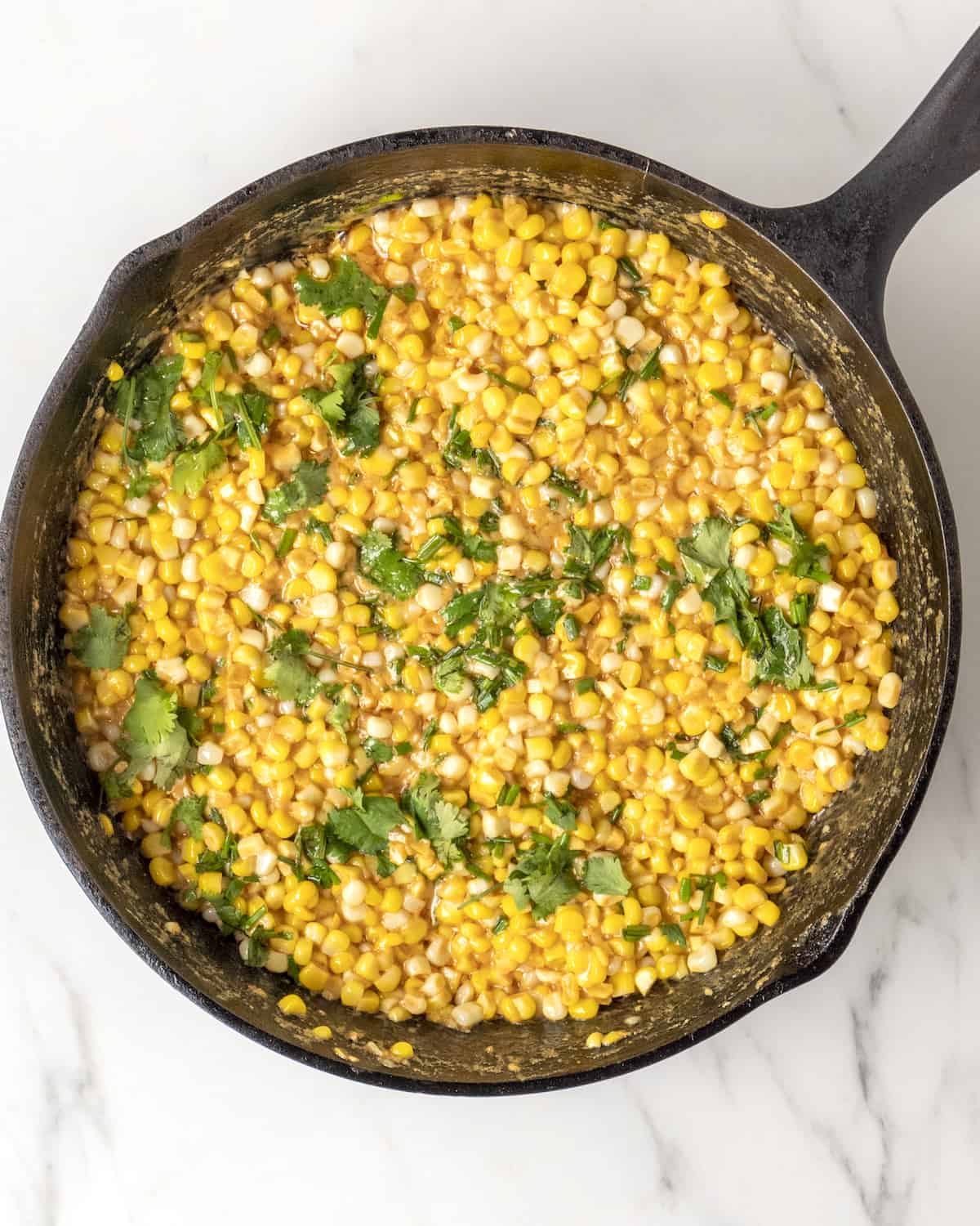 The final dish of cooked corn with all ingredients incorporated into it topped with fresh cilantro and chives.