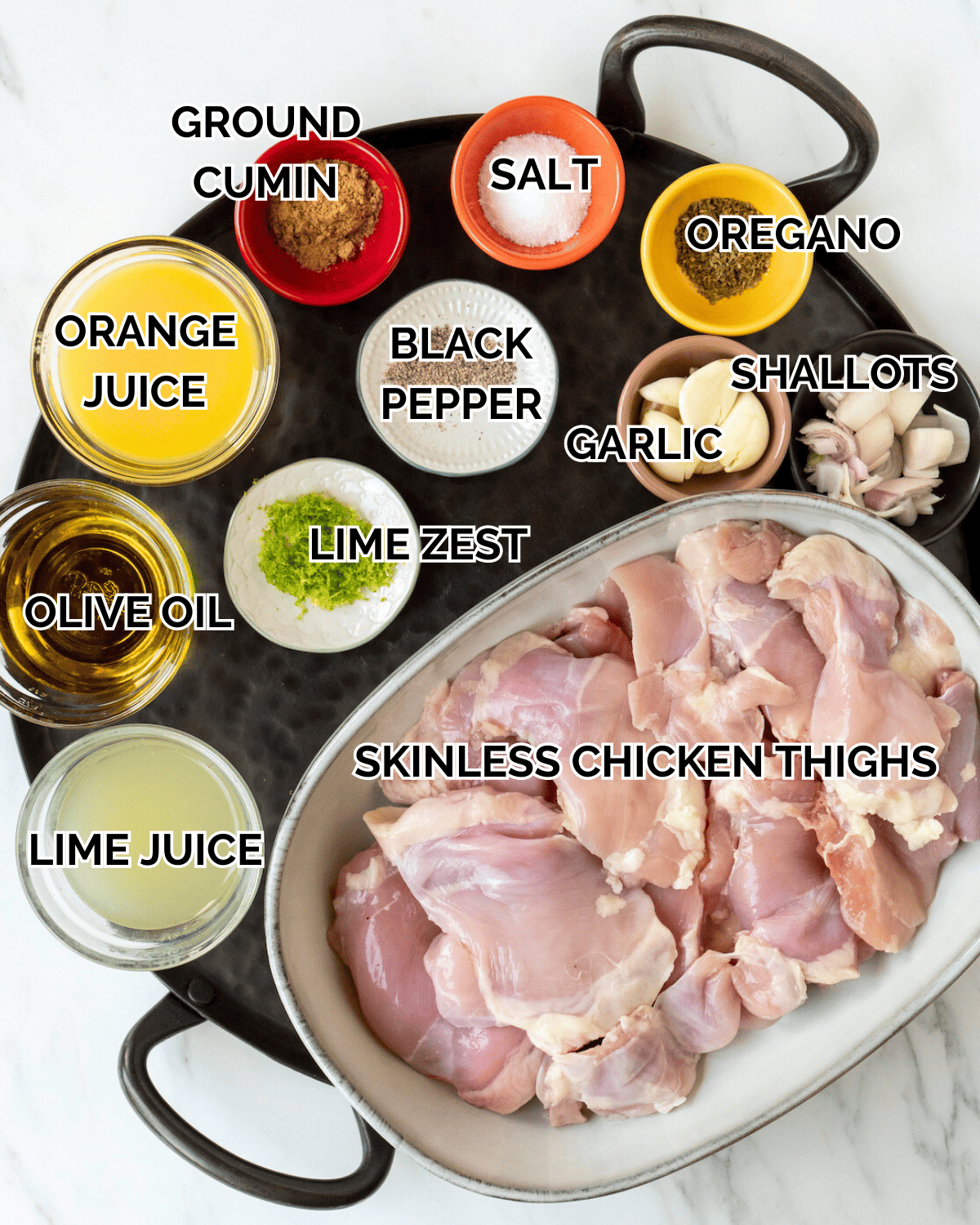 A plate that has all the ingredients in tiny prep bowls.  The ingredients displayed are Ground Cumin, Salt, Oregano, Black Pepper, Garlic, Shallots, Lime Zest, Orange Juice, Olive Oil, Lime Juice, and Chicken Thighs. 