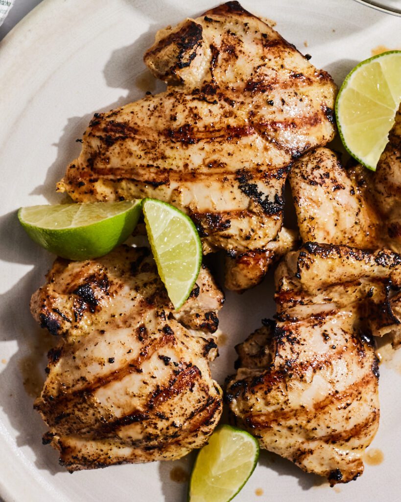 Several pieces of the cuban mojo chicken are sitting on a plate with some lime wedges.  