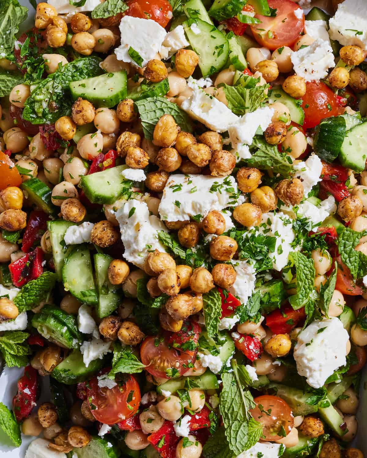 A close-up shot of chickpea chopped salad, with crispy chickpeas, mint leaves, feta, cucumbers, tomatoes and red bell peppers.