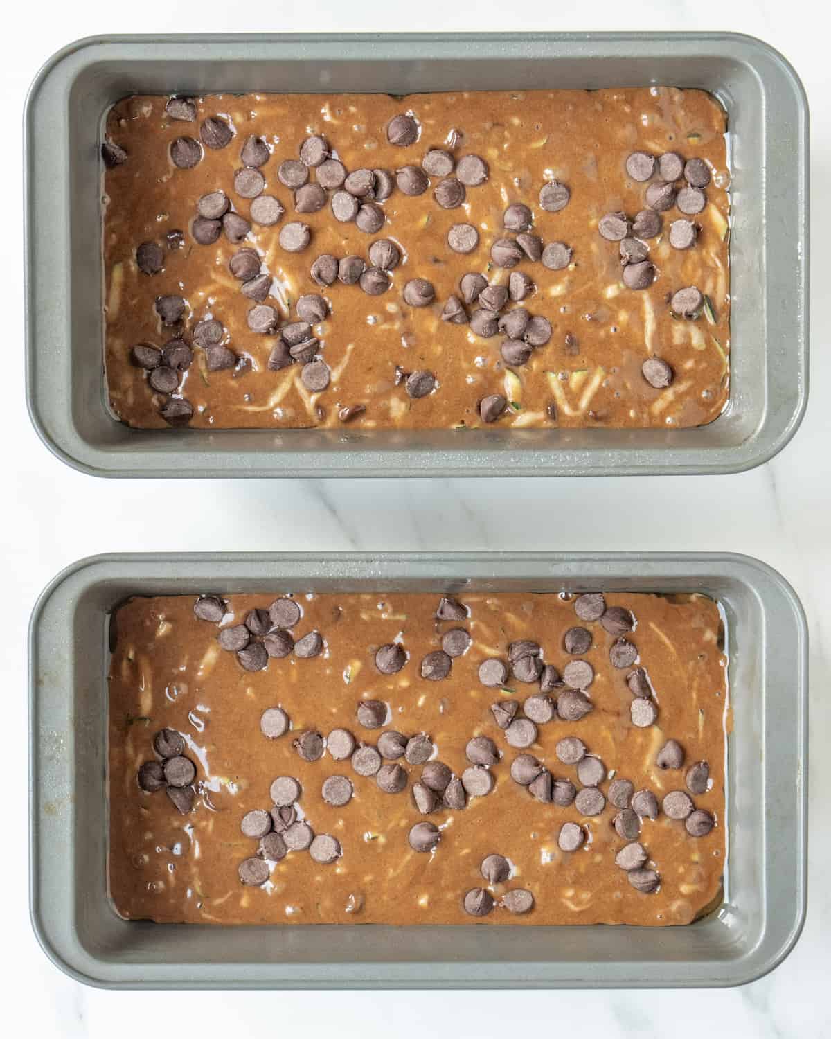 Two loaf pans with double chocolate chip zucchini bread batter topped with more chocolate chips.