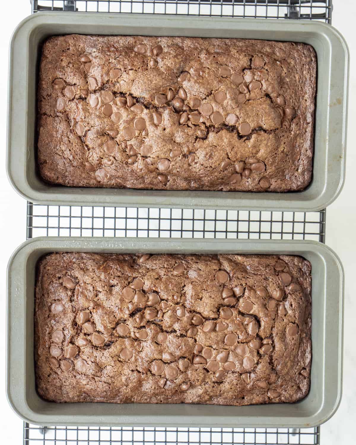 Two loaf pans on a wire rack with baked double chocolate chip zucchini bread.