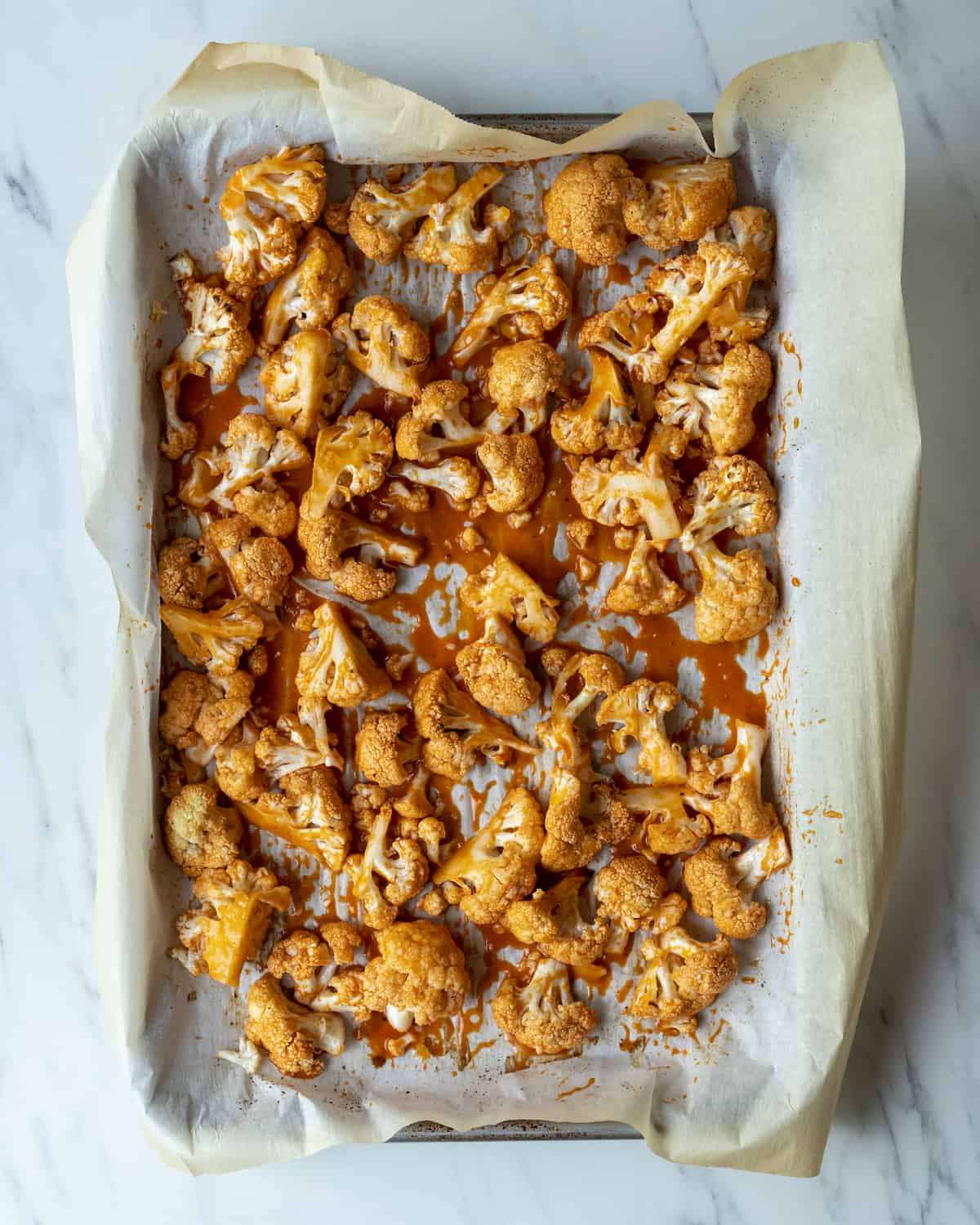 A parchment lined baking sheet with roasted cauliflower tossed with buffalo sauce.