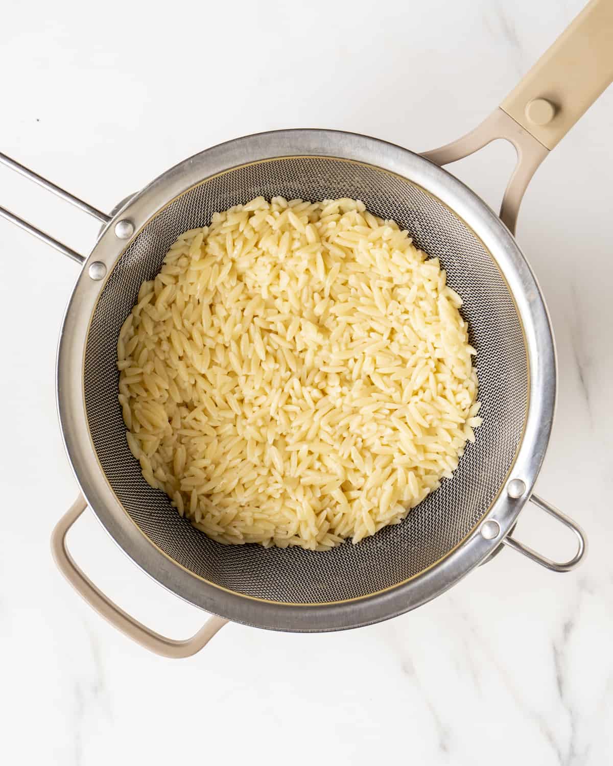 Cooked orzo in a strainer in a pot.