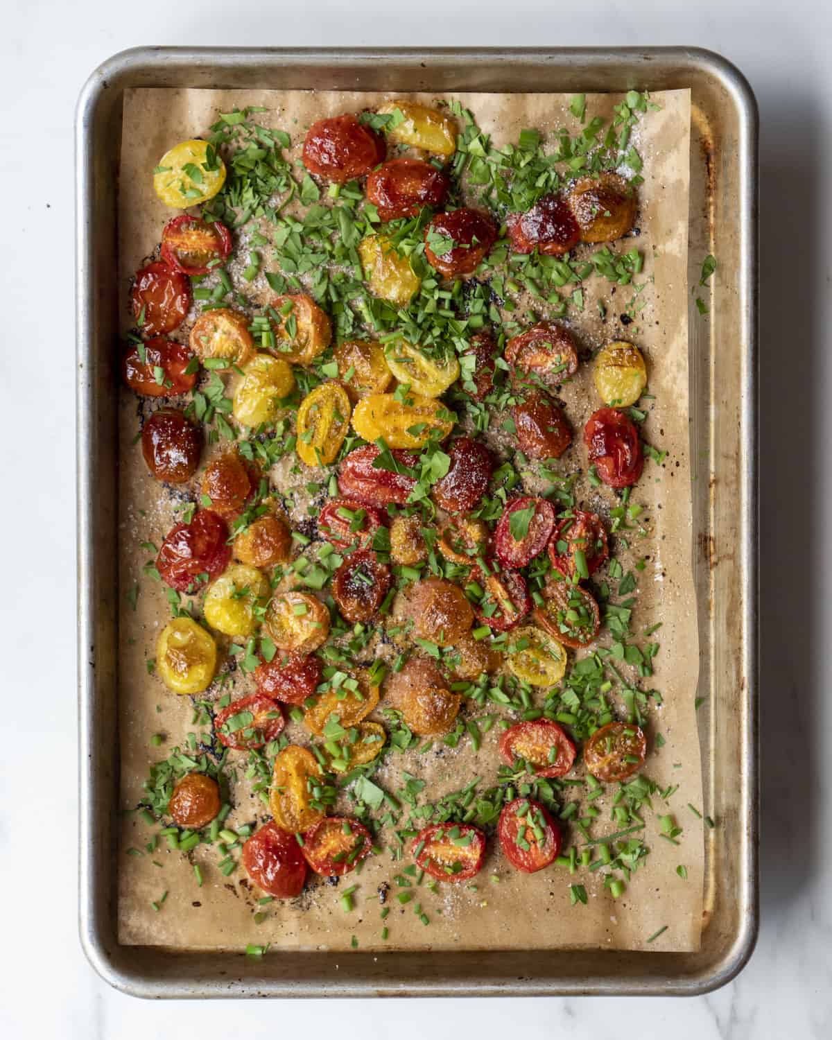 Parchment lined sheet pan with roasted tomatoes topped with herbs.