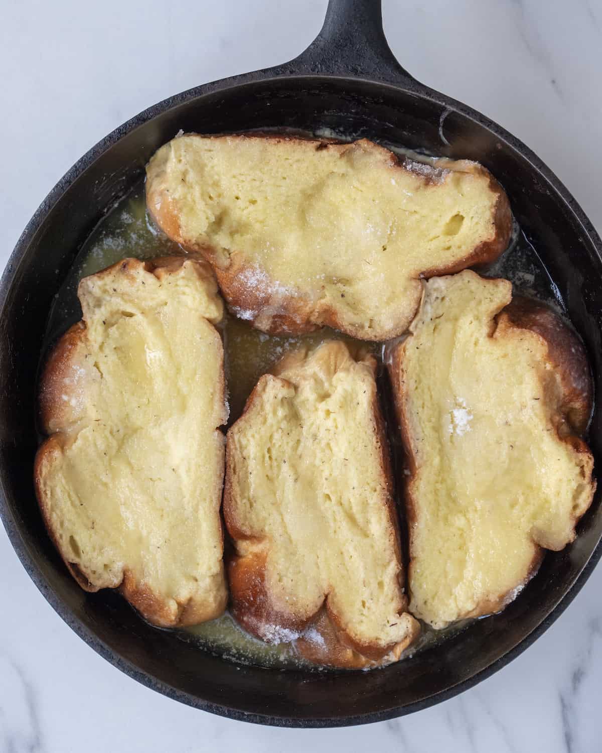 Bread slices soaked into french toast batter being cooked on a skillet.