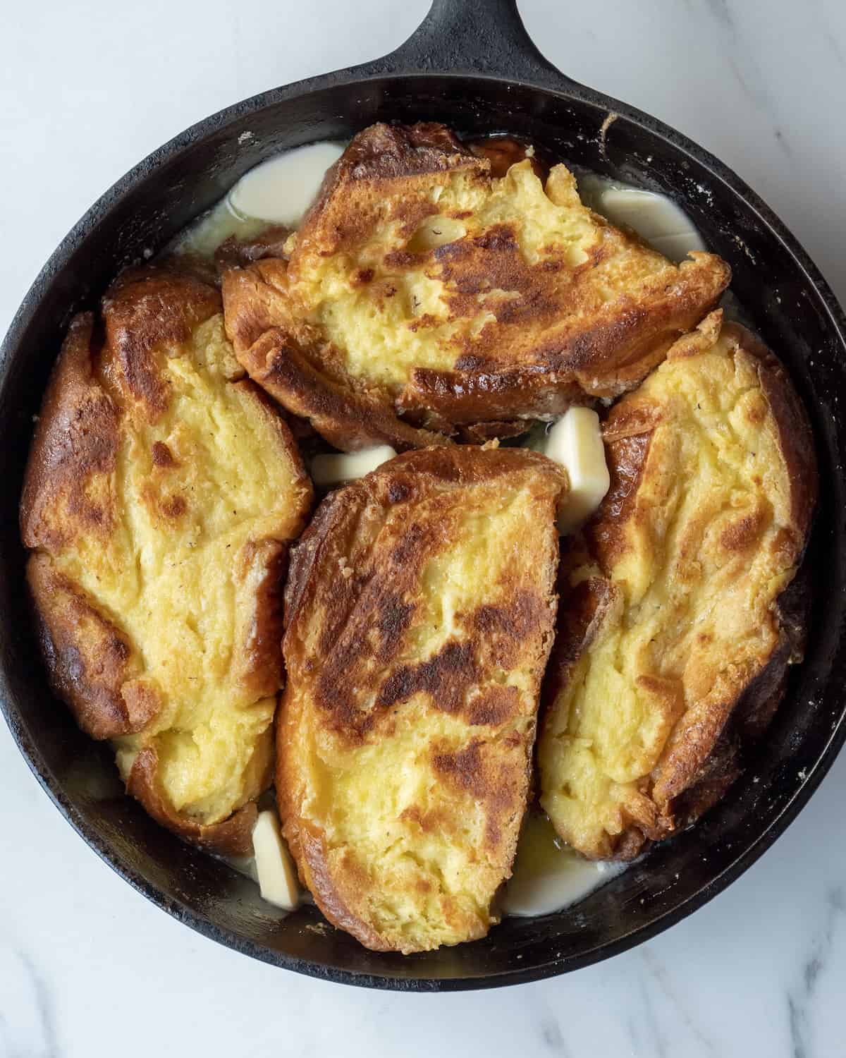 Skillet with bread slices soaked into french toast batter cooked on one side along with butter on the base of the skillet.