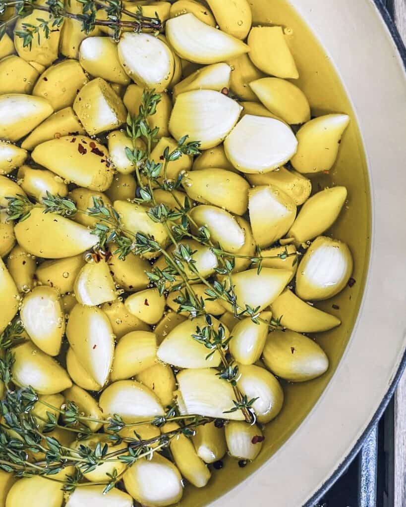 Lots of garlic cloves starting to roast while sitting in a brasier full of olive oil and thyme.