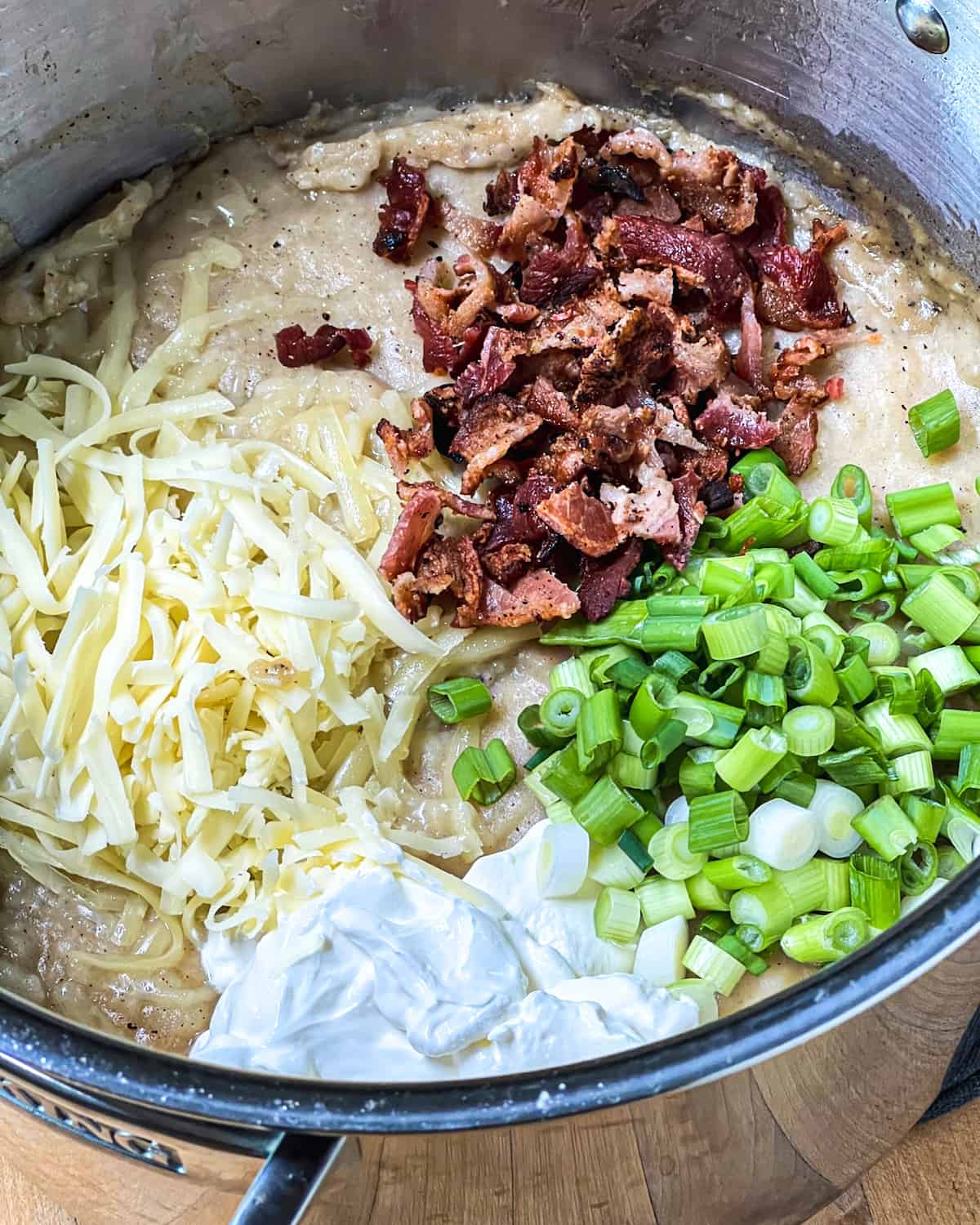 After adding the insides of the diced baked potato, add the crumbled bacon, cheddar cheese, scallions and sour cream into the pot of potato soup.