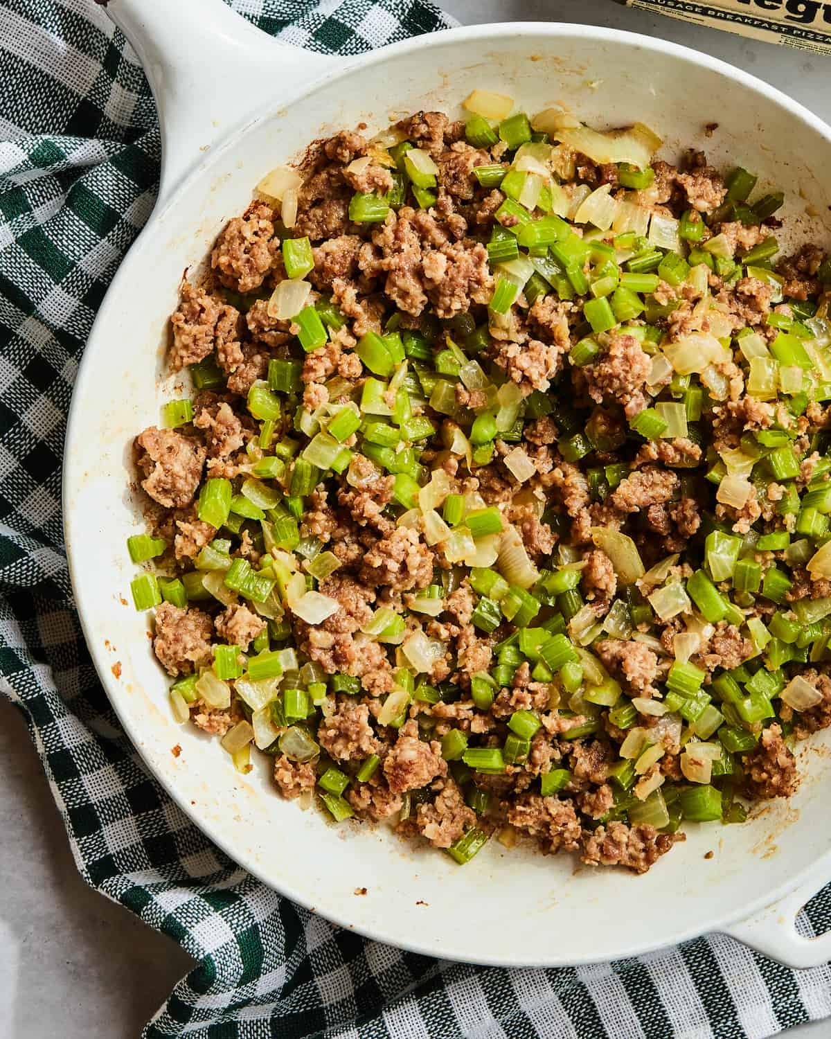 A white pan with ground sausage, celery and onion cooked together placed on a kitchen towel.