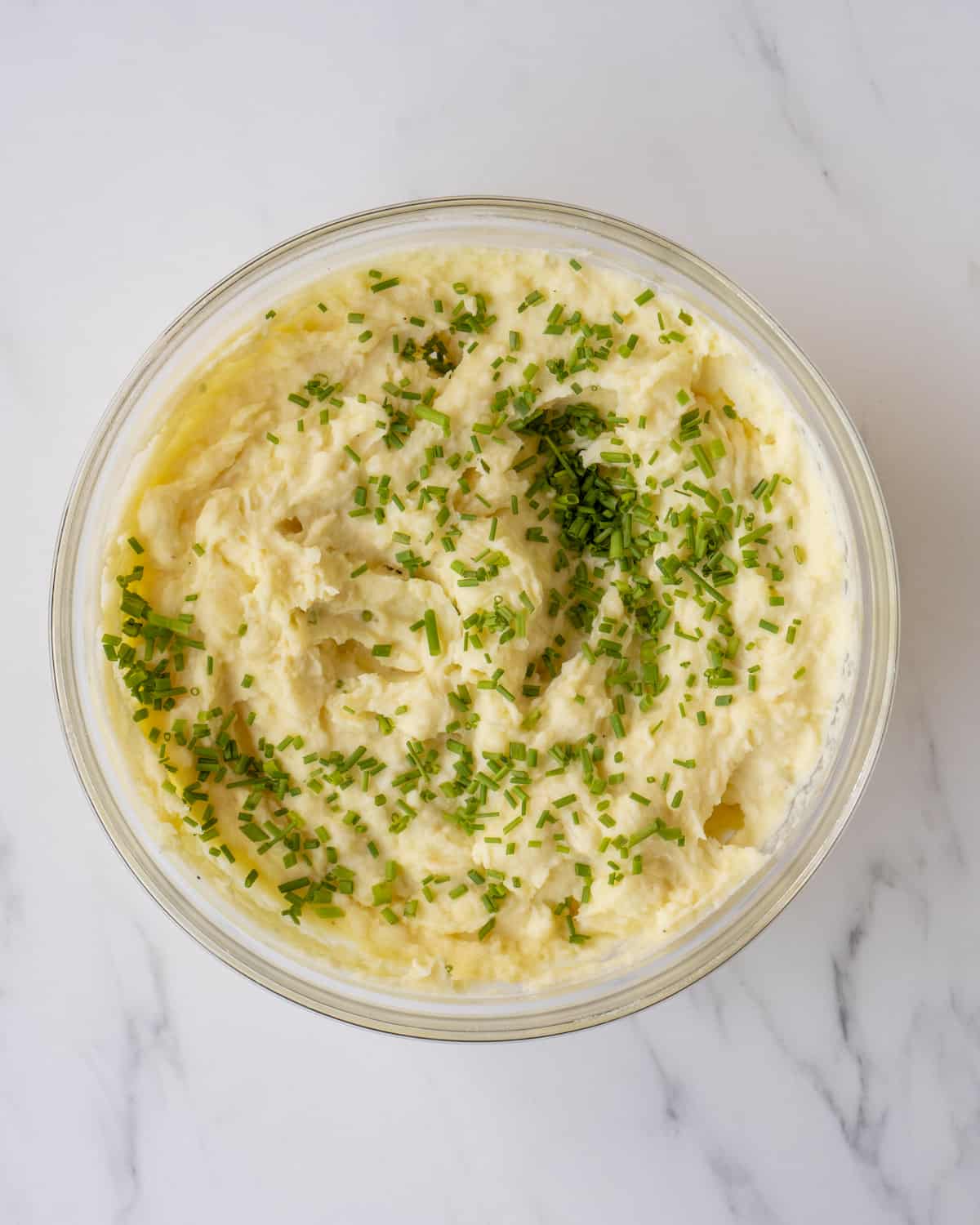 The finished dish of mashed potatoes sitting in a glass bowl with chopped up chives.  