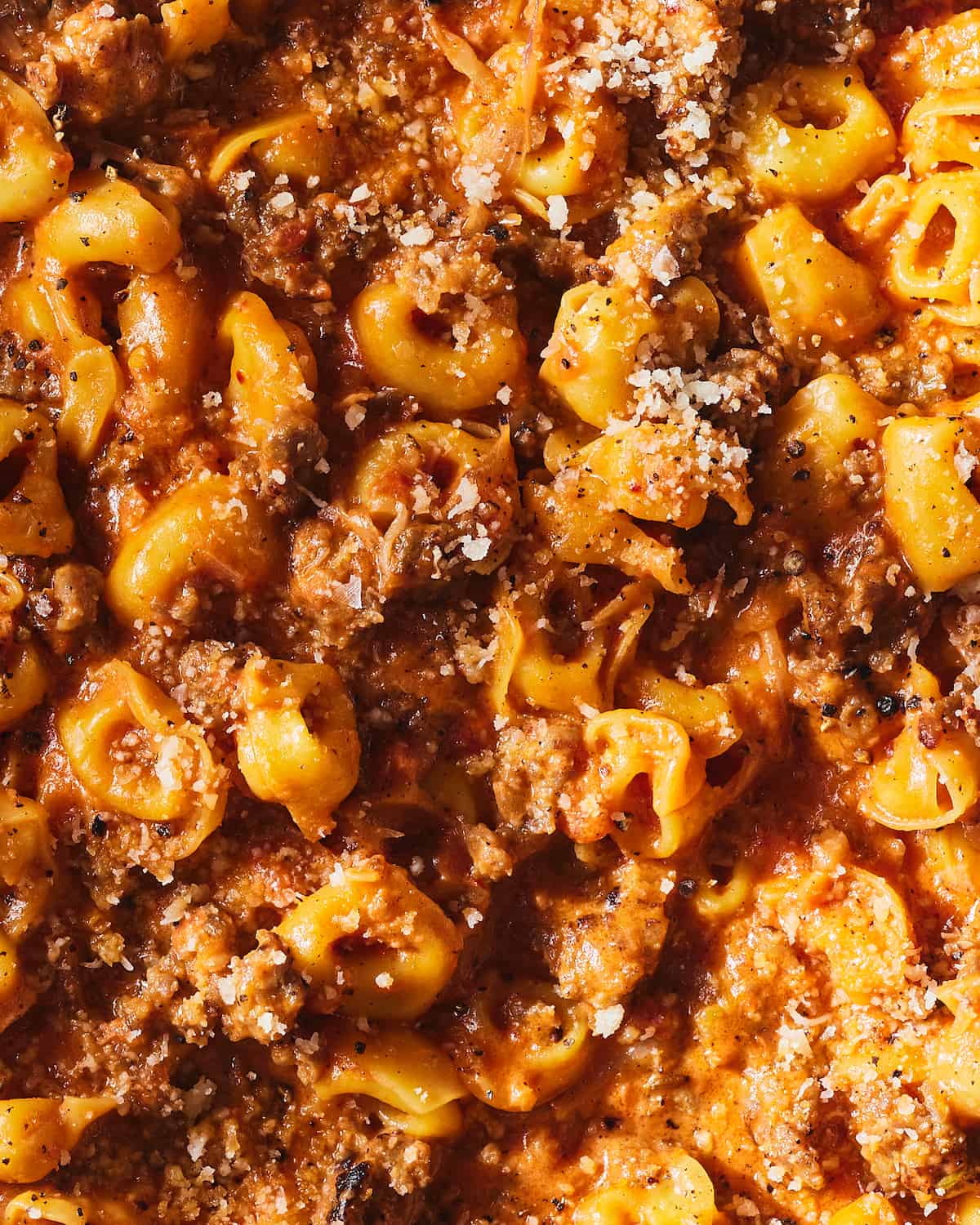 A tight shot of tortellini in a glossy red sauce that has crumbled Italian sausage and mascarpone. It's garnished with freshly grated parmesan cheese.