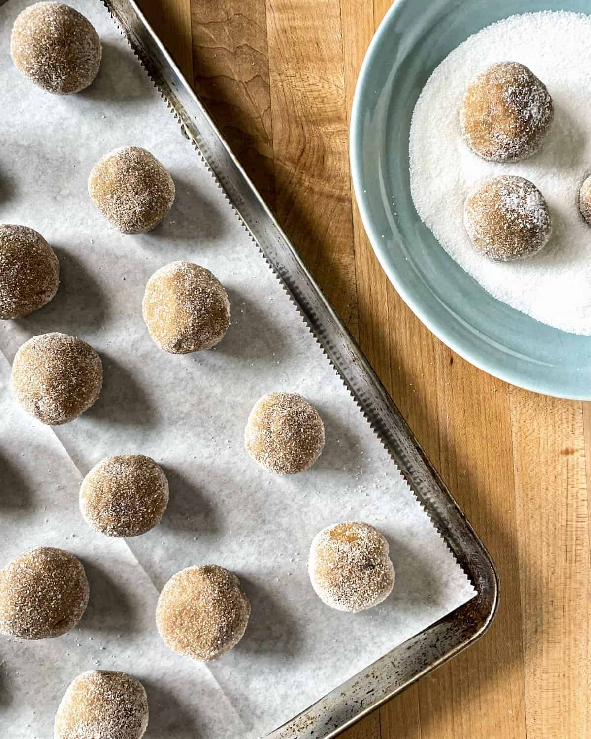 Molasses Cookie dough rolled out in 2 tablespoon sized balls then rolled in sugar and placed on on a piece of parchment paper on a baking sheet