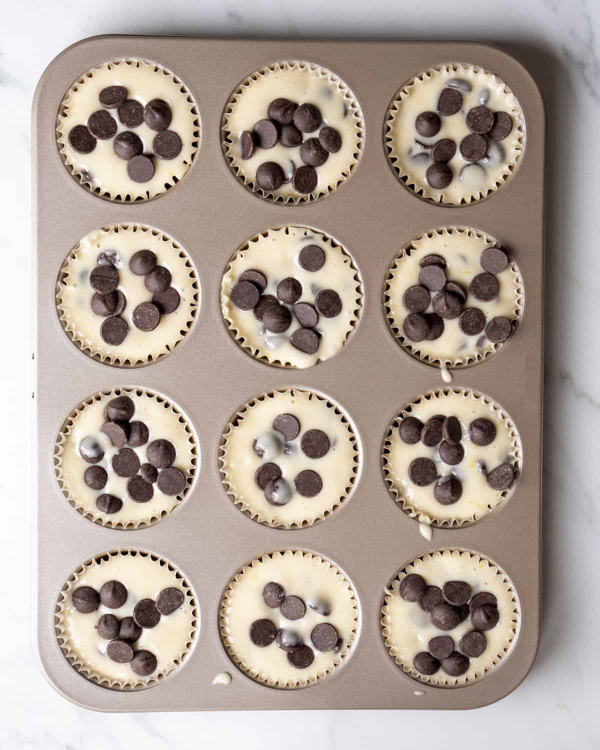 A 3x4 muffin tin has been filled with the mixture and chocolate chips.  