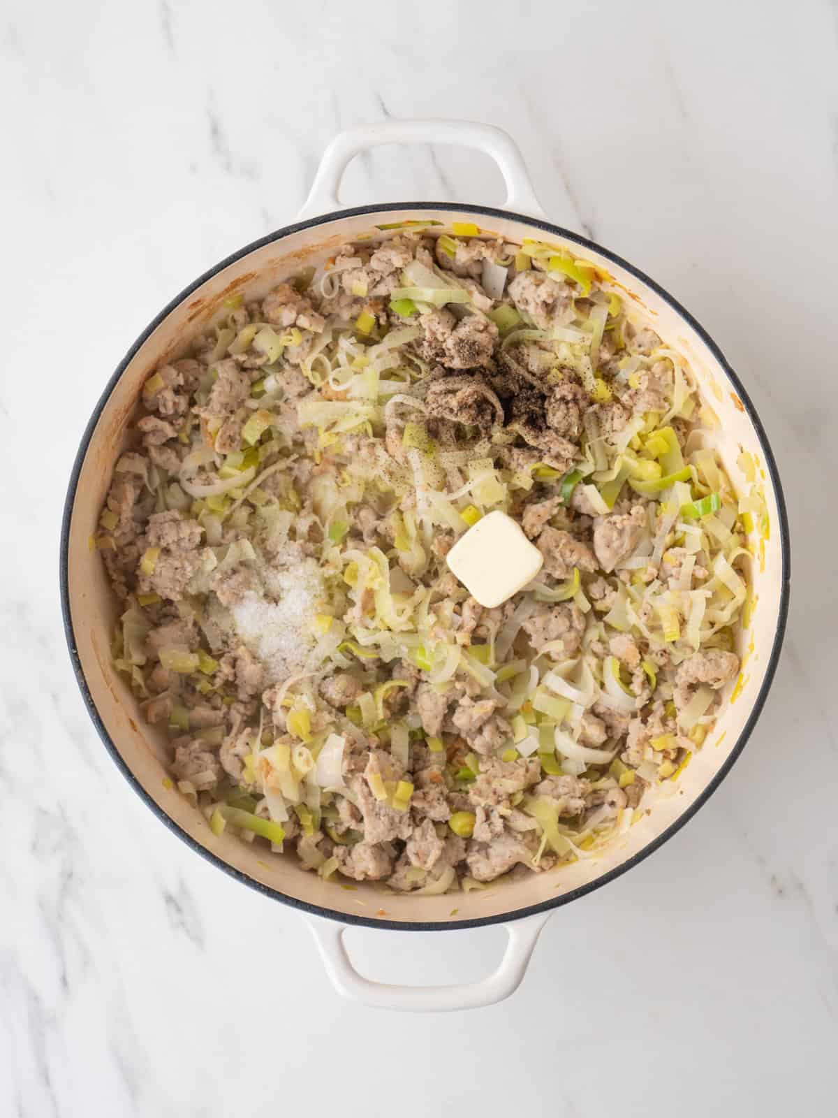 A dutch oven with sausage, leeks and butter added along with salt and pepper.